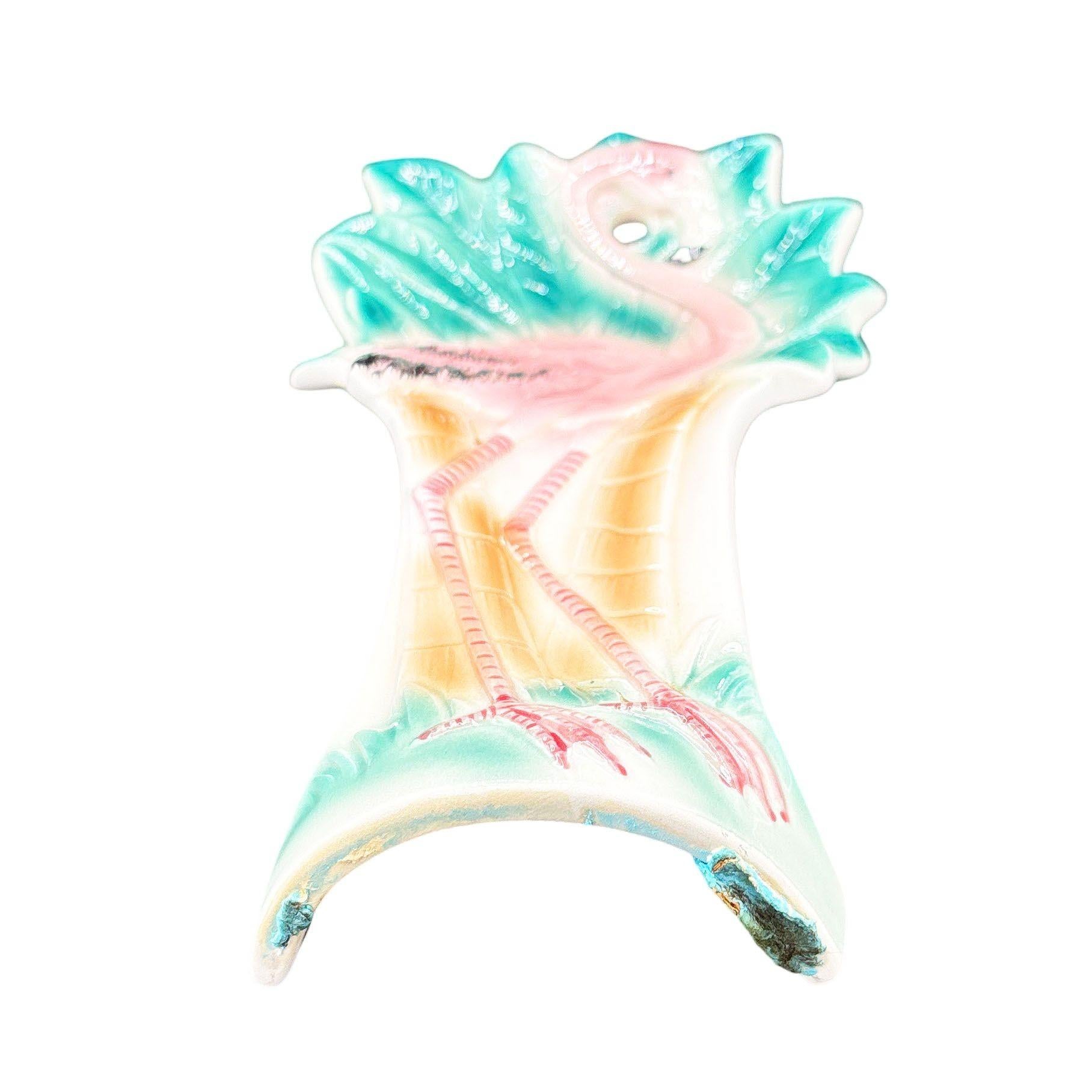 Repose-cuillère moderniste en céramique rose et verte Flamingo par Sarsaparilla Deco. Le repose-cuillère représente un flamant rose détaillé avec de longues pattes, une forme mince et haute se tenant sur un champ herbeux, la poitrine fièrement