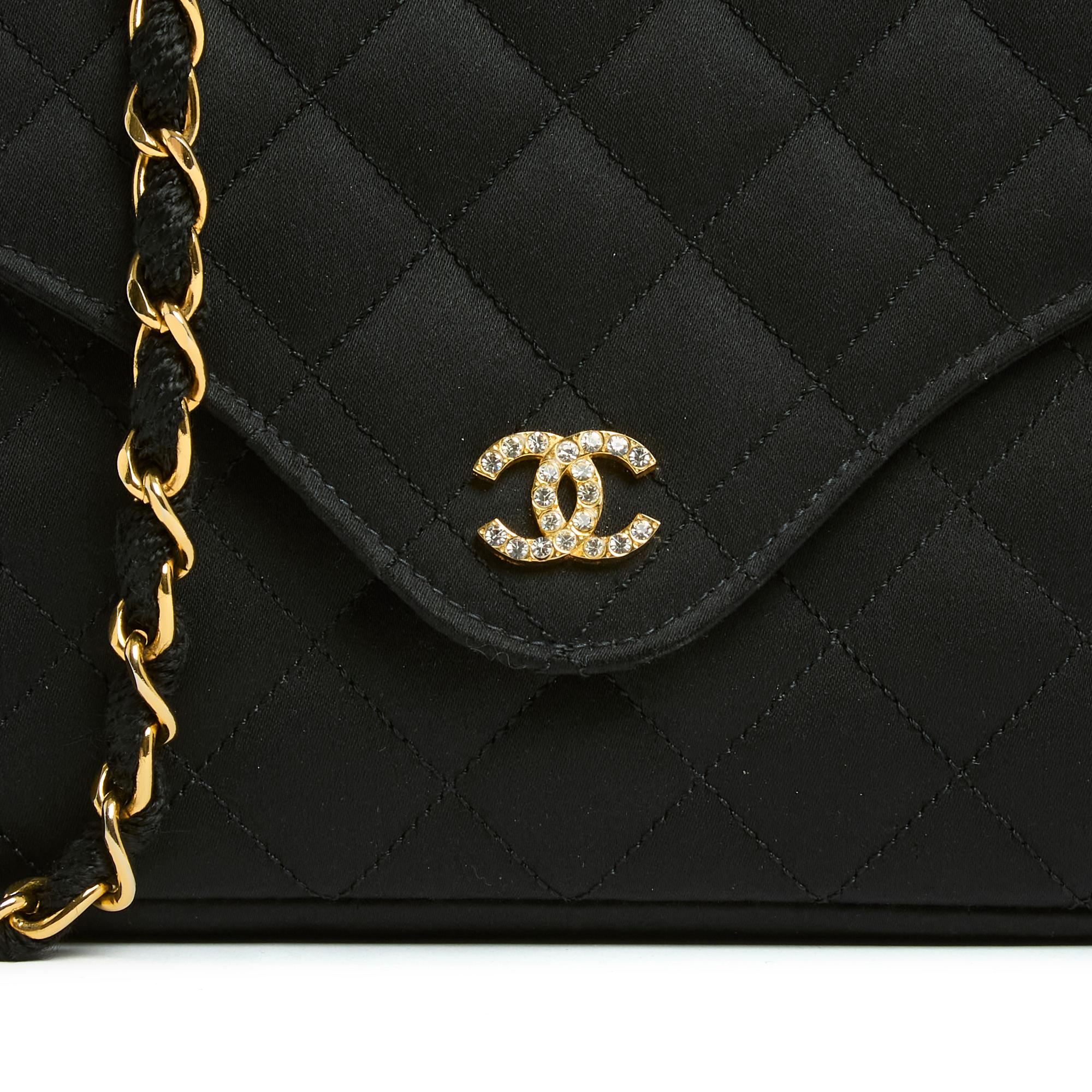 Small Chanel bag from the Timeless or Classic series in quilted black silk satin, a simple flap on the top closed with a snap surmounted by a CC logo inlaid with white rhinestones, interior coordinated with a patch pocket, gold metal chain shoulder