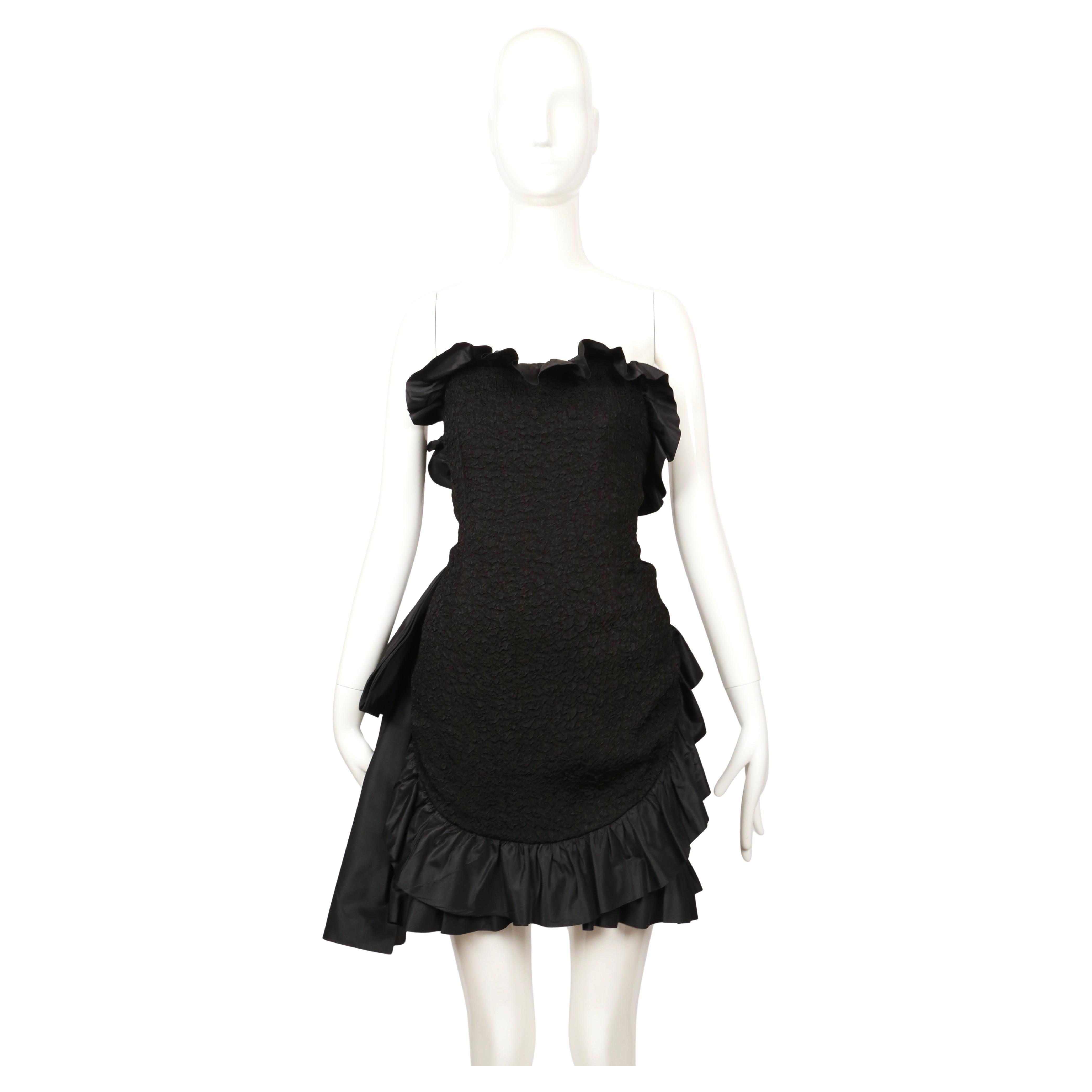 Raro vestido de cóctel sin tirantes diseñado por Yves Saint Laurent que data de la colección de otoño de 1987. La pieza está fabricada con un tejido negro texturizado con un sutil dibujo en relieve, que le confiere una gran profundidad. Presenta una