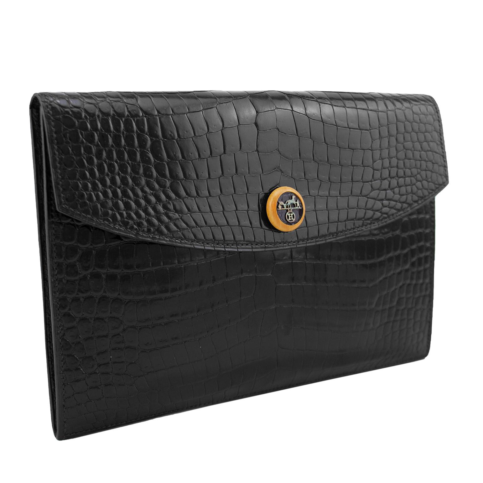 Classic and elegant black crocodile effect Hermes Rio clutch from 1988. Envelope style with a single wood round button snap button closure embellished with an H and equestrian logo. Single large supple black leather interior compartment. Dates from
