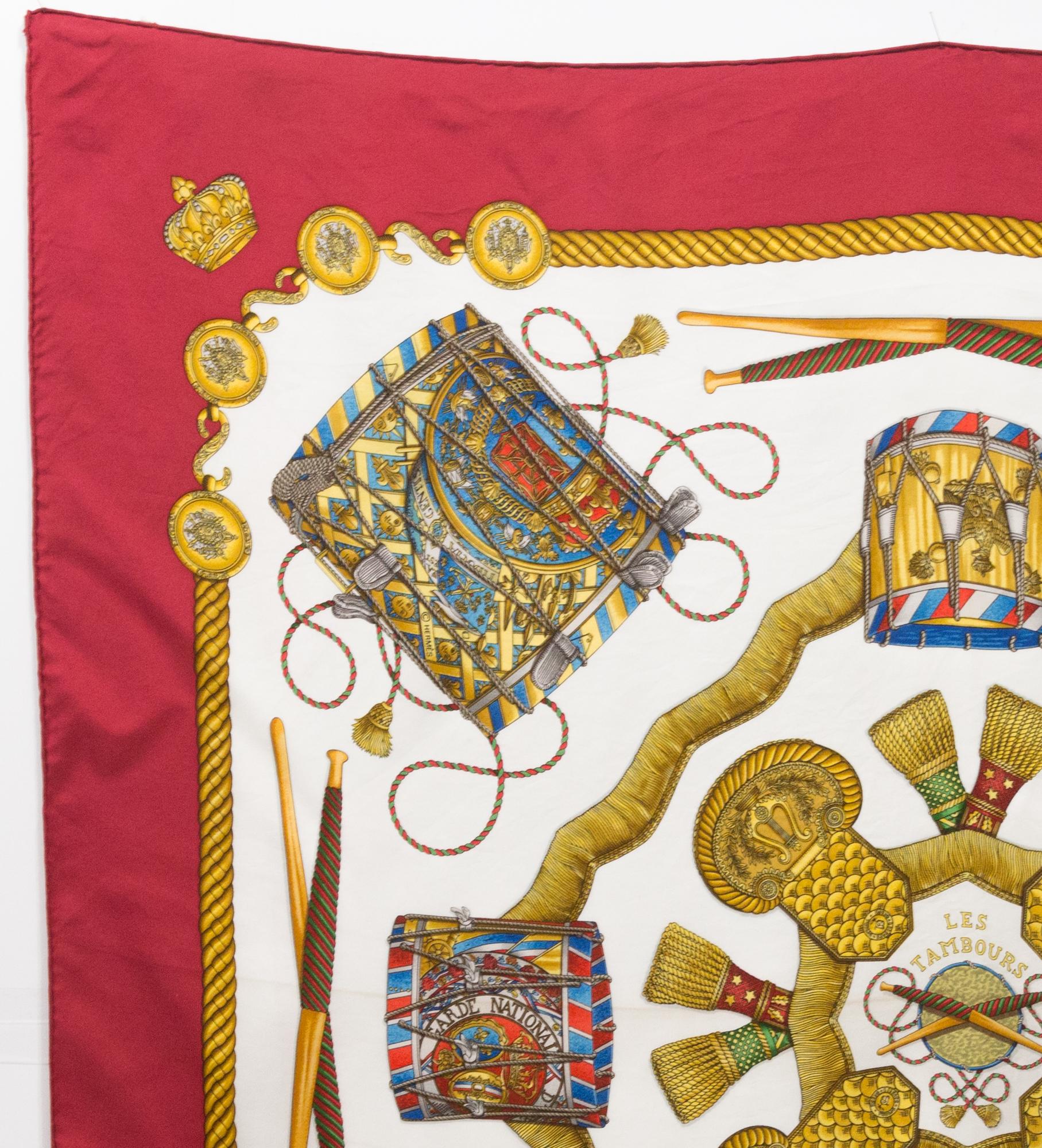 Hermes silk scarf « Les Tambours » by Joachim Metz  featuring a deep red border and a Hermès signature. 
Circa 1989
In good vintage condition. Made in France.
35,4in. (90cm)  X 35,4in. (90cm)
We guarantee you will receive this  iconic item as