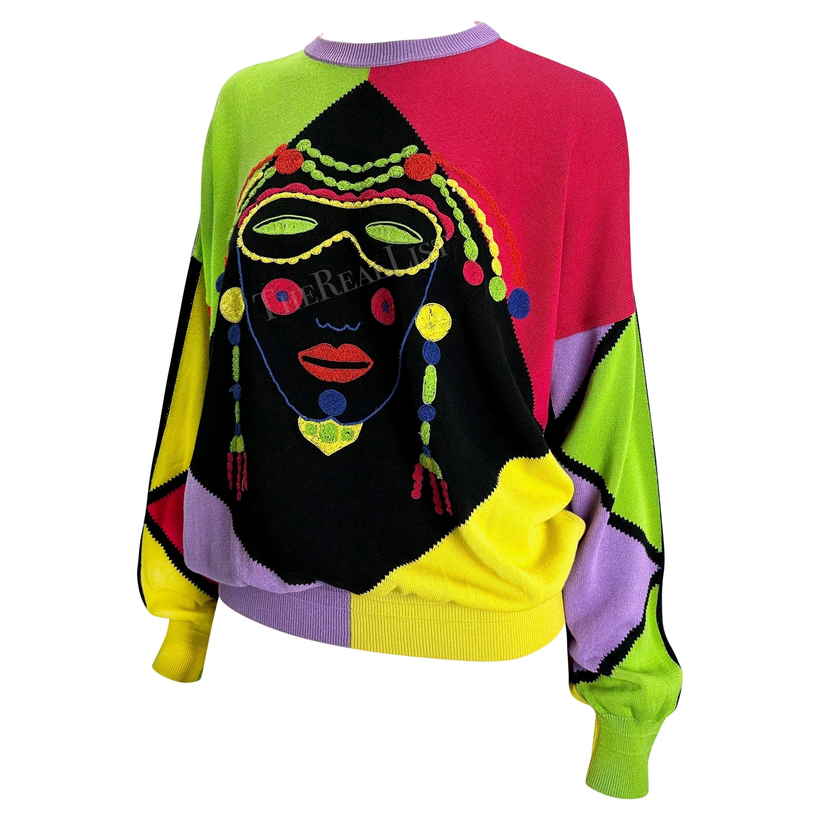 Wir präsentieren einen mehrfarbigen, bestickten Gianni Versace Pullover, entworfen von Gianni Versace. Dieser übergroße Pullover aus dem Jahr 1990 zeichnet sich durch ein Farbblockmuster mit einem aufgestickten Harlekin-Gesicht auf der Vorderseite