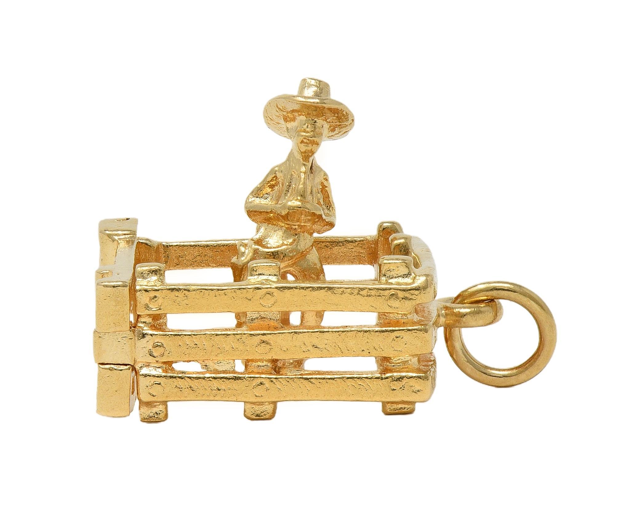 Designed as a highly rendered farmer wearing cowboy hat
Depicted standing in a wooden fence pen
With a functional hinged gate
Inscribed 'Don't Fence Me In'
Completed by jump ring bale
Stamped for 14 karat gold
Circa: 1990s
Measures: 13/16 x 9/16