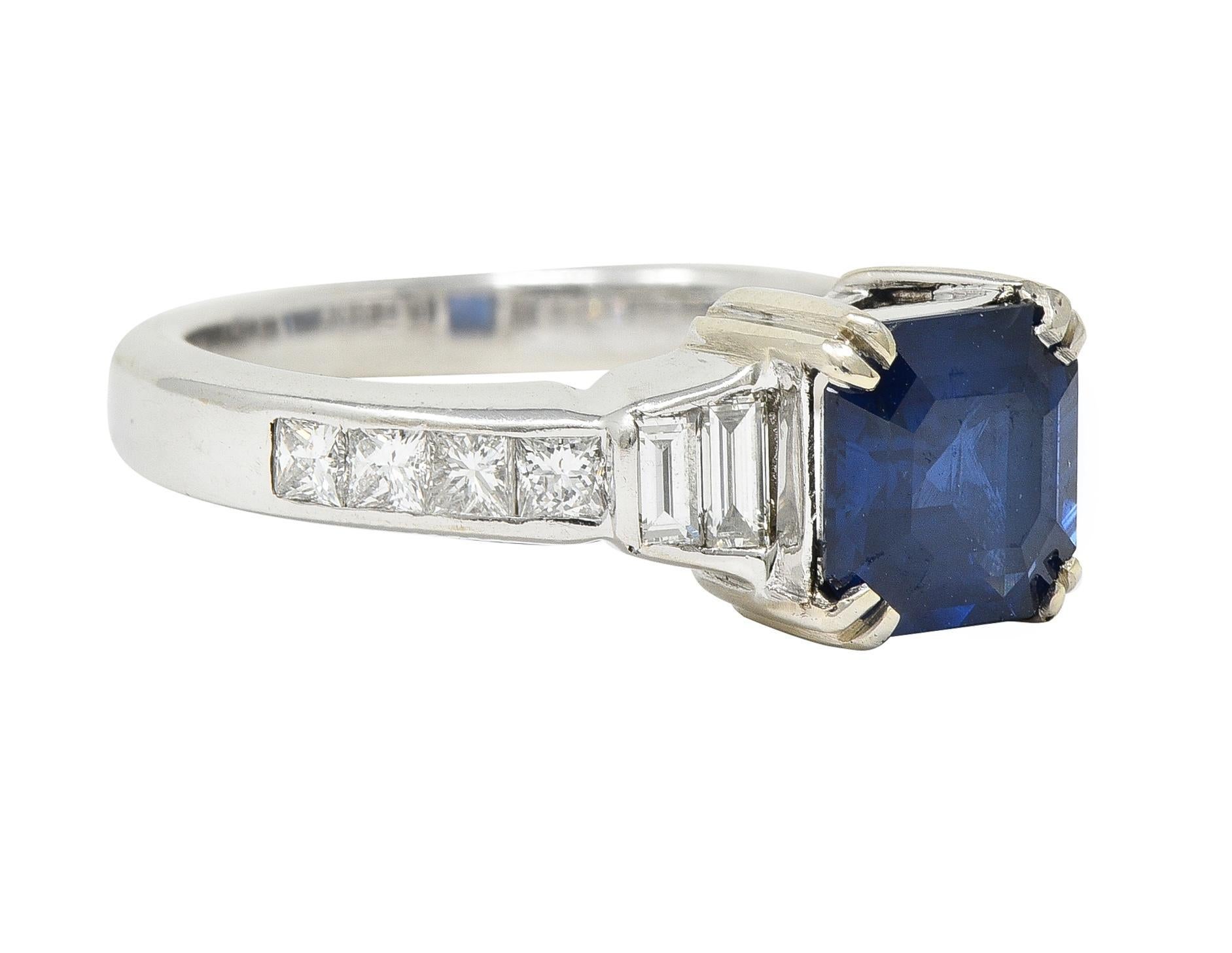 Centering an asscher cut sapphire weighing 1.95 carats total - transparent dark blue in color 
Natural Thai in origin - set with split prongs in basket and flanked by stepped shoulders
Bar set with baguette cut diamonds weighing approximately 0.36