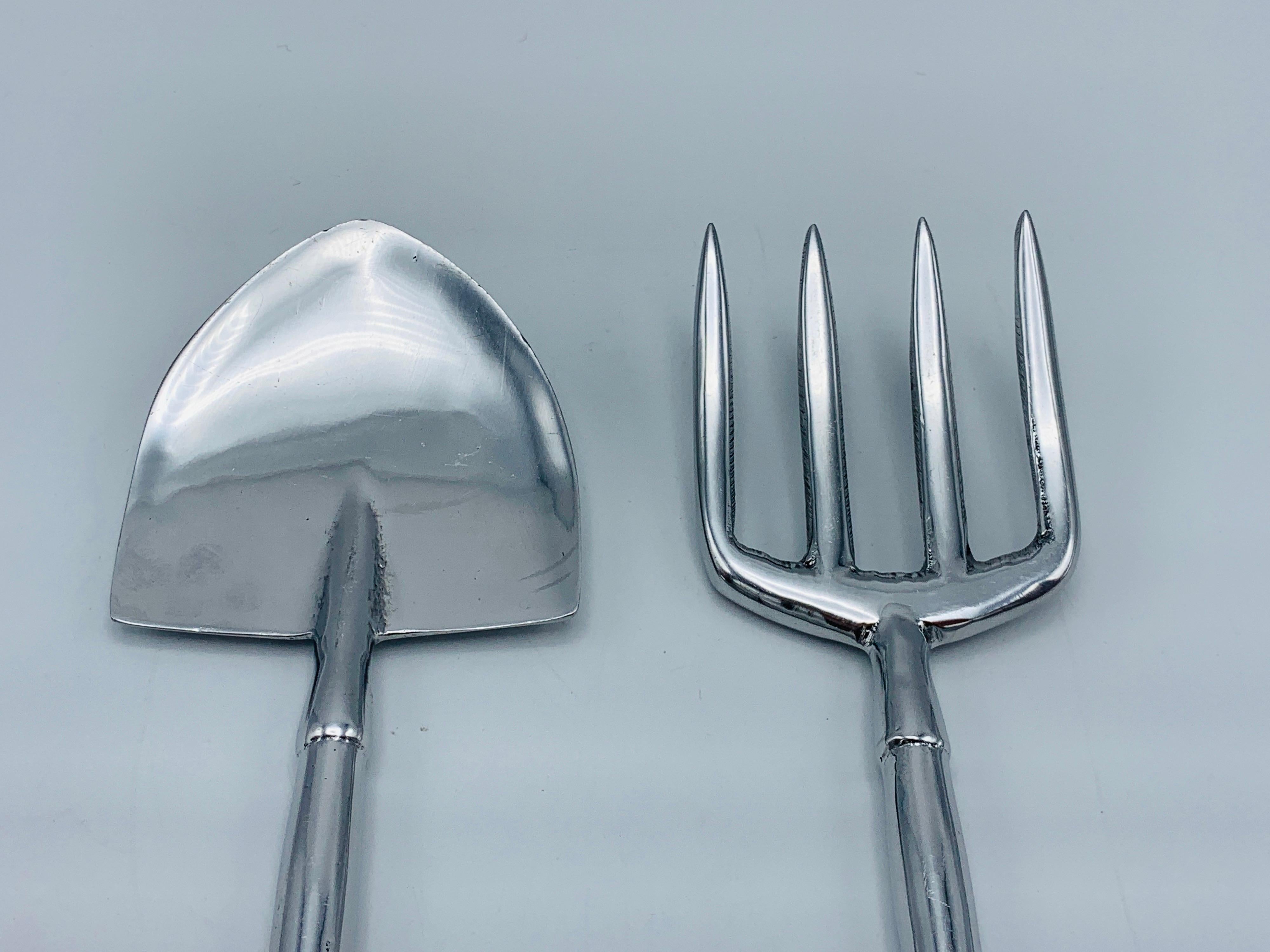 Offered is a pair of 1990s aluminum, garden tools shaped salad utensils. The shovel and pitchfork utensil set have been freshly polished and cleaned, giving a vibrant glow to the material. Marked '1995, Mariposa' on backside of each, see last two