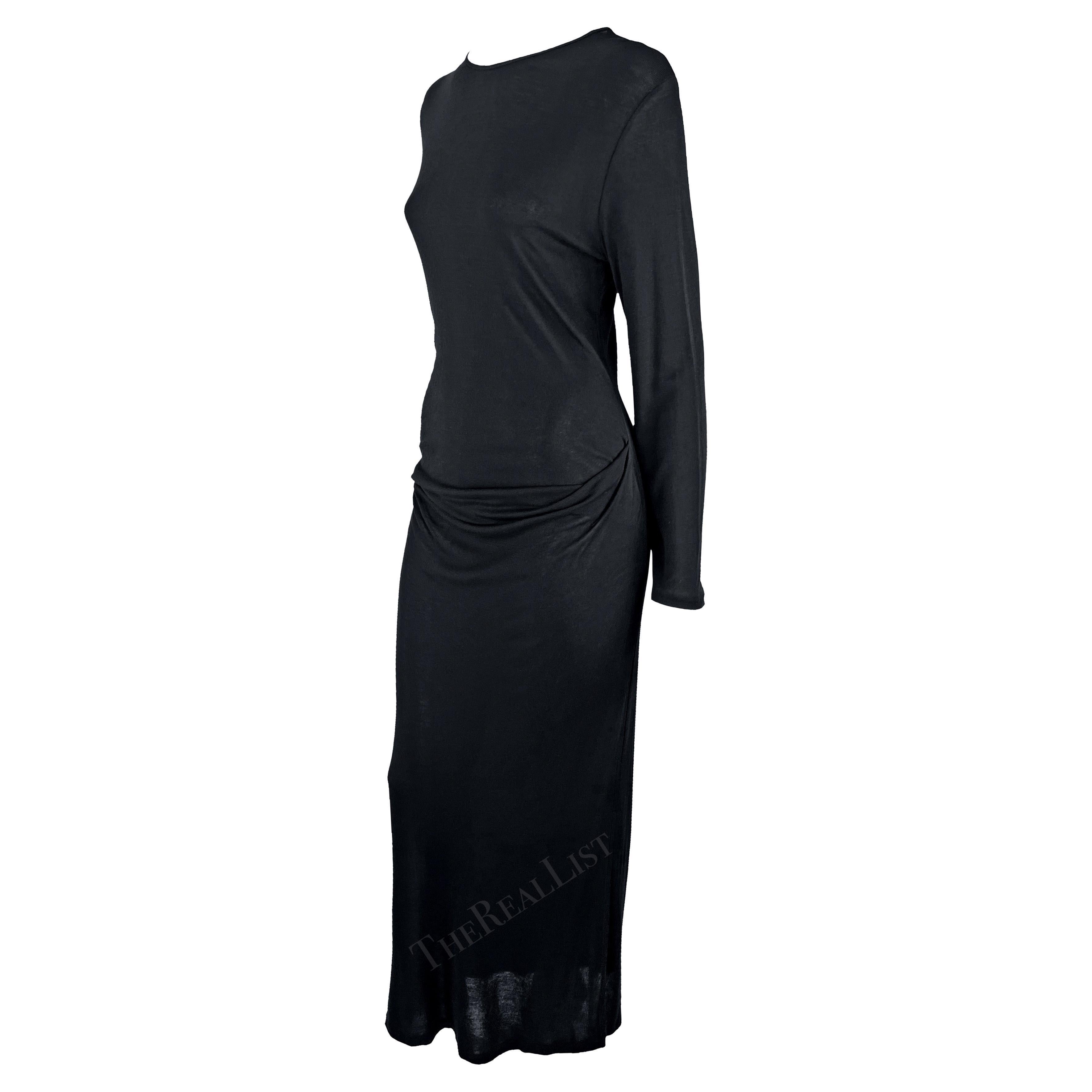 Présentation d'une robe chic en tricot noir Ann Demeulemeester. Datant des années 1990, cette robe de sol très légèrement transparente comporte des manches longues et est complétée par un léger froncement au niveau des hanches. Cette robe sombre et