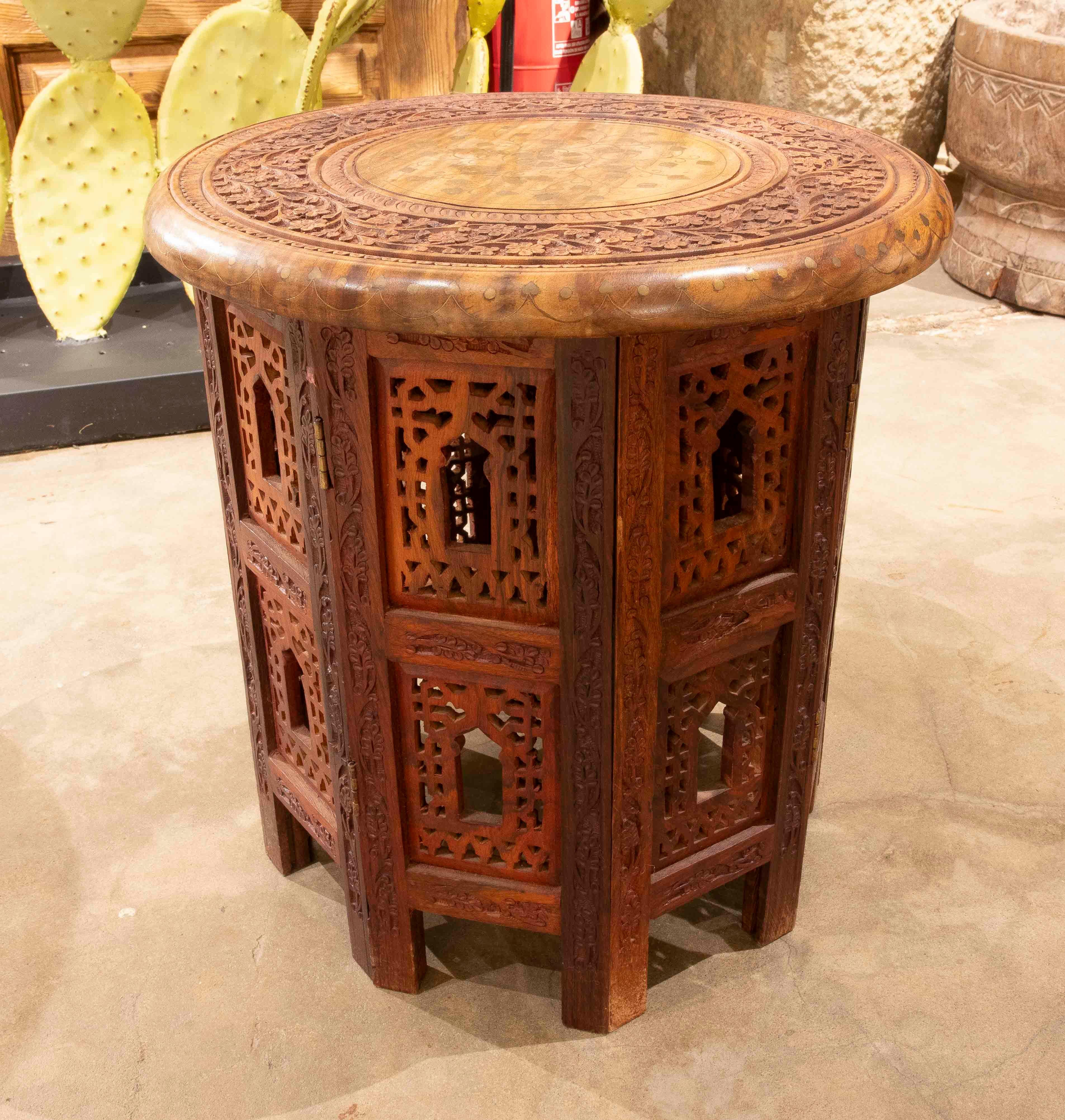 Une élégante table d'appoint arabe en bois massif, sculptée à la main, présentant des motifs géométriques et floraux complexes inspirés de l'architecture islamique. Son design octogonal et son ajourage sur les panneaux latéraux évoquent l'artisanat