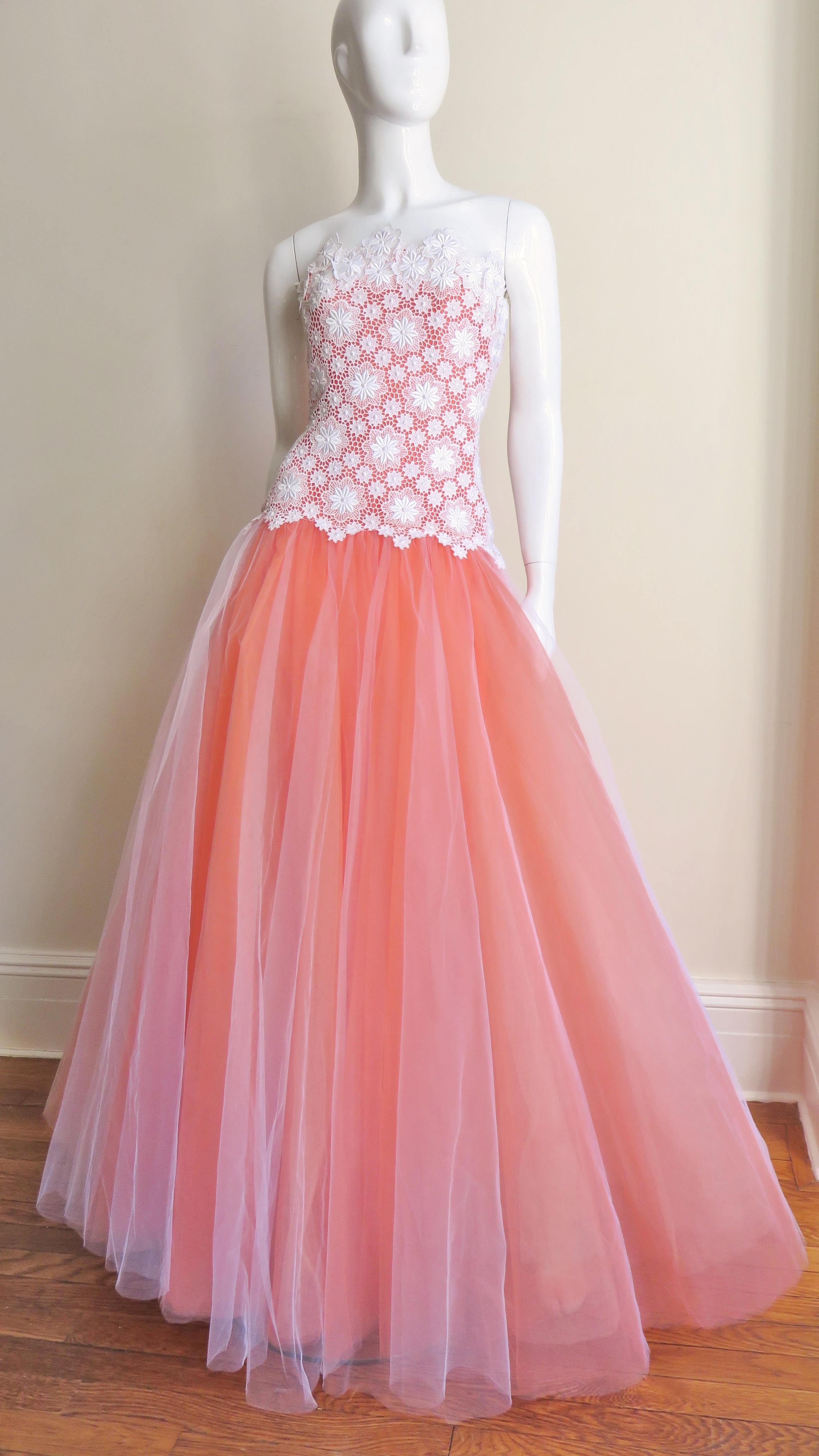 A fabulous gown from Arnold Scaasi in coral and white.  It is strapless with a fitted, boned, hip length bodice of white lace with flower appliques.  The magnificent tulle skirt emanates from under the scalloped edges of the bodice at the hips and