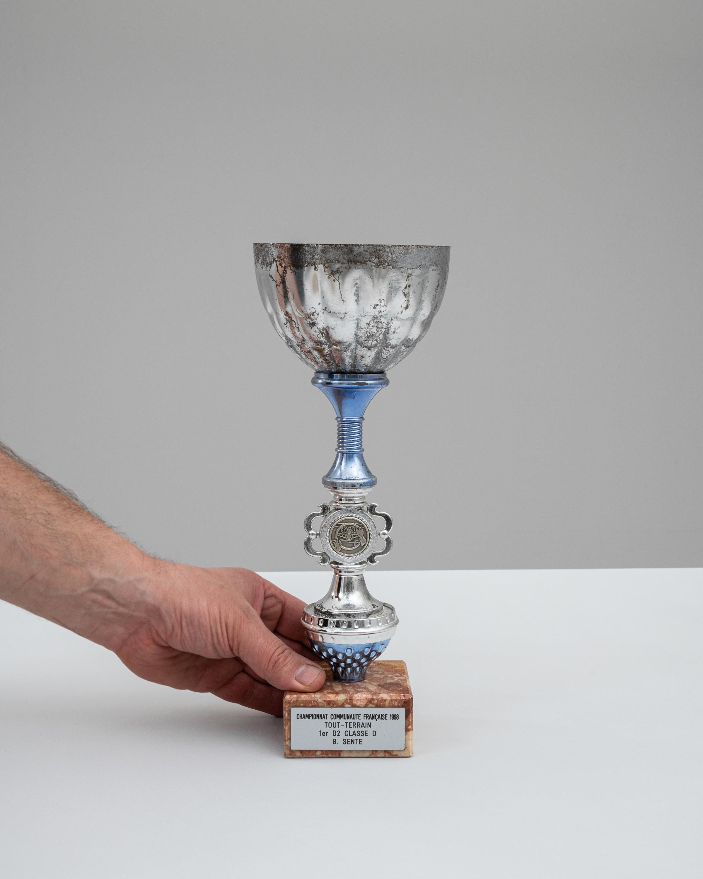 Ce gobelet belge en métal et marbre des années 1990 est un hommage emblématique aux triomphes de la course tout-terrain, marquant un moment victorieux du championnat Tout-Terrain de 1998. Le gobelet lui-même présente une silhouette classique, avec