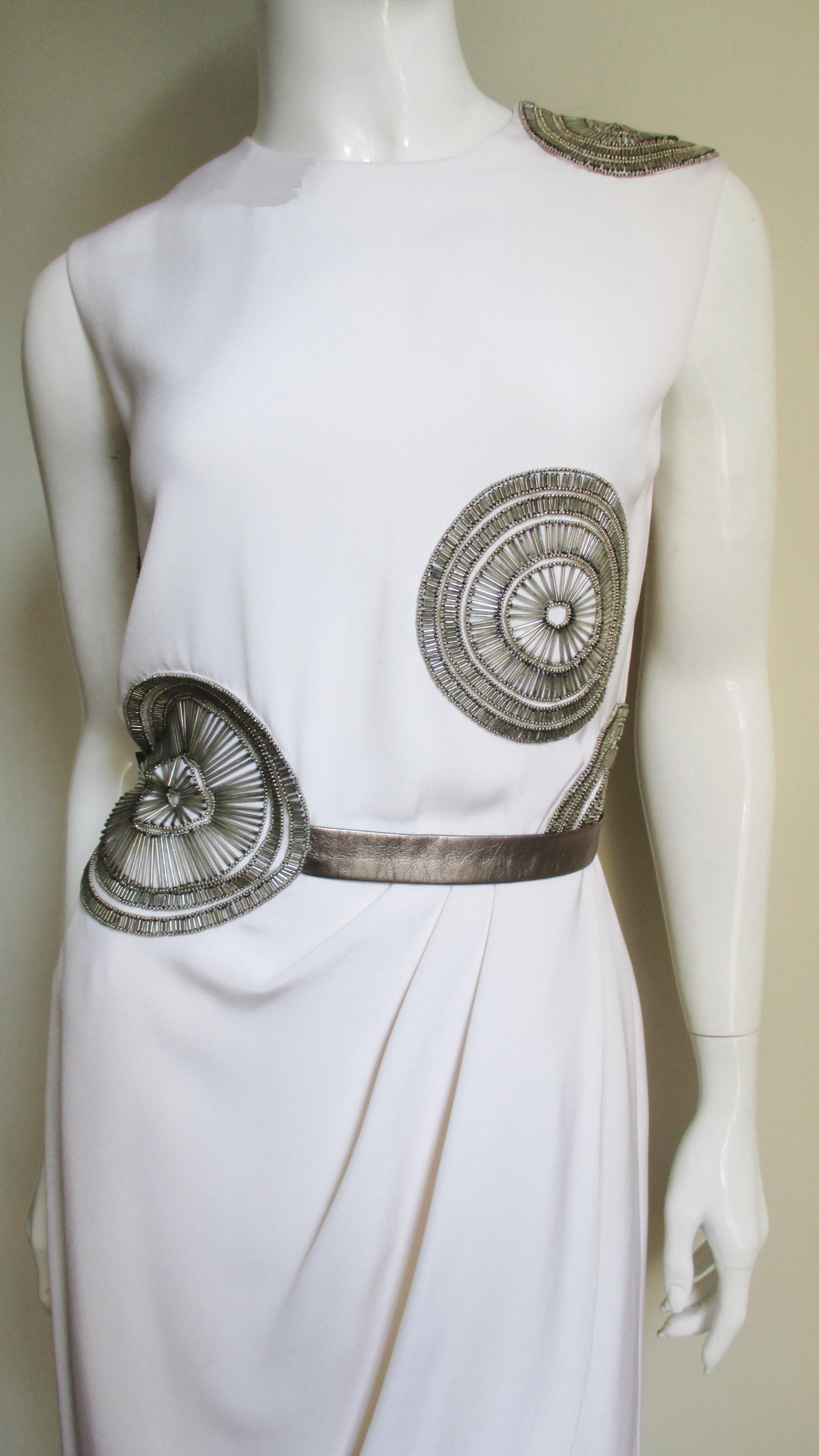 A beautiful white silk dress with elaborately detailed silver glass tubular and gold seed beaded circles on the bodice by Bill Blass. The dress is sleeveless with a bronze leather belt and straight skirt which overlaps and drapes in the front.  It