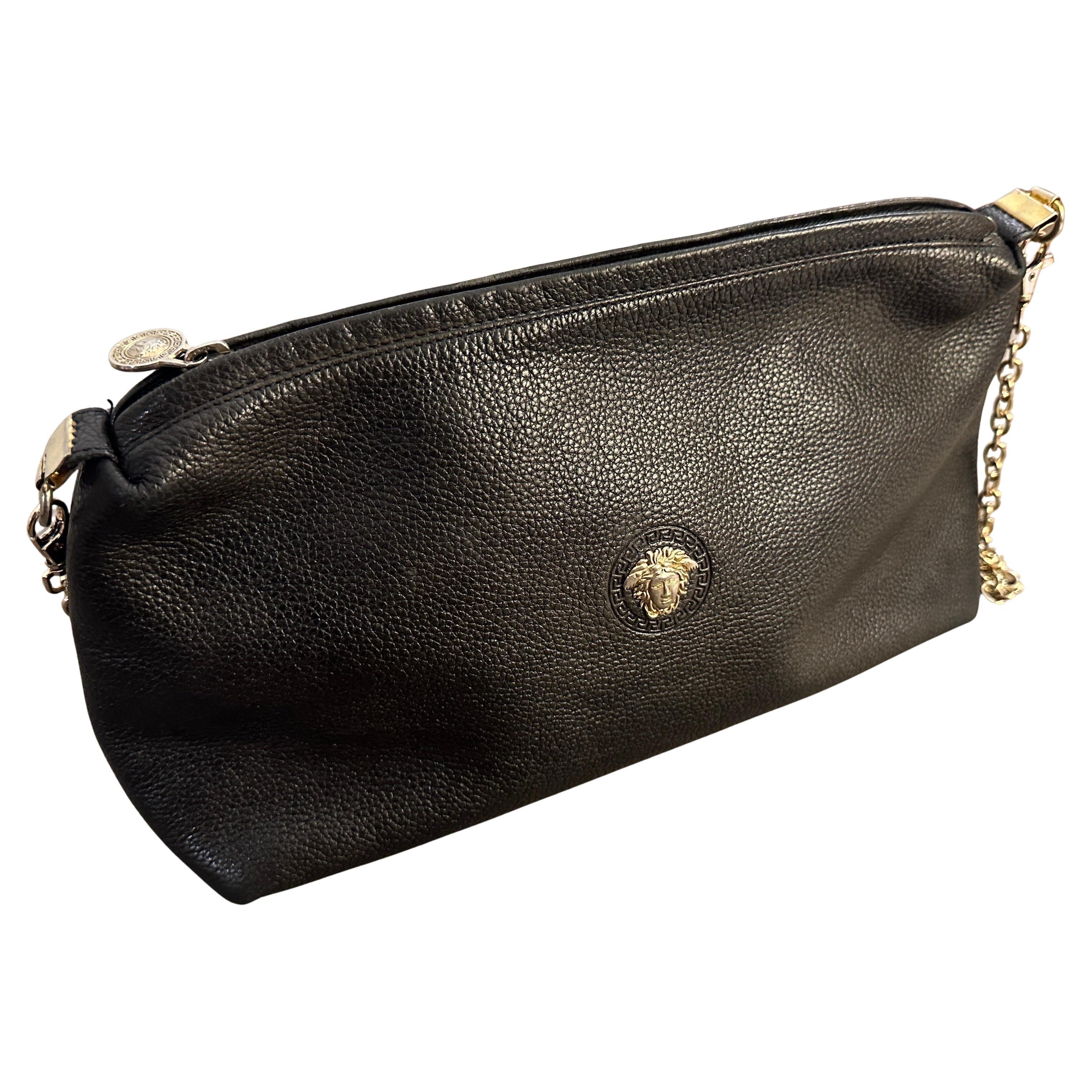 This is a sleek and sophisticated 1990s black leather bag designed by Gianni Versace. The bag features a minimalistic yet luxurious aesthetic, crafted from high-quality textured black leather. At its center, it boasts the iconic Medusa head emblem