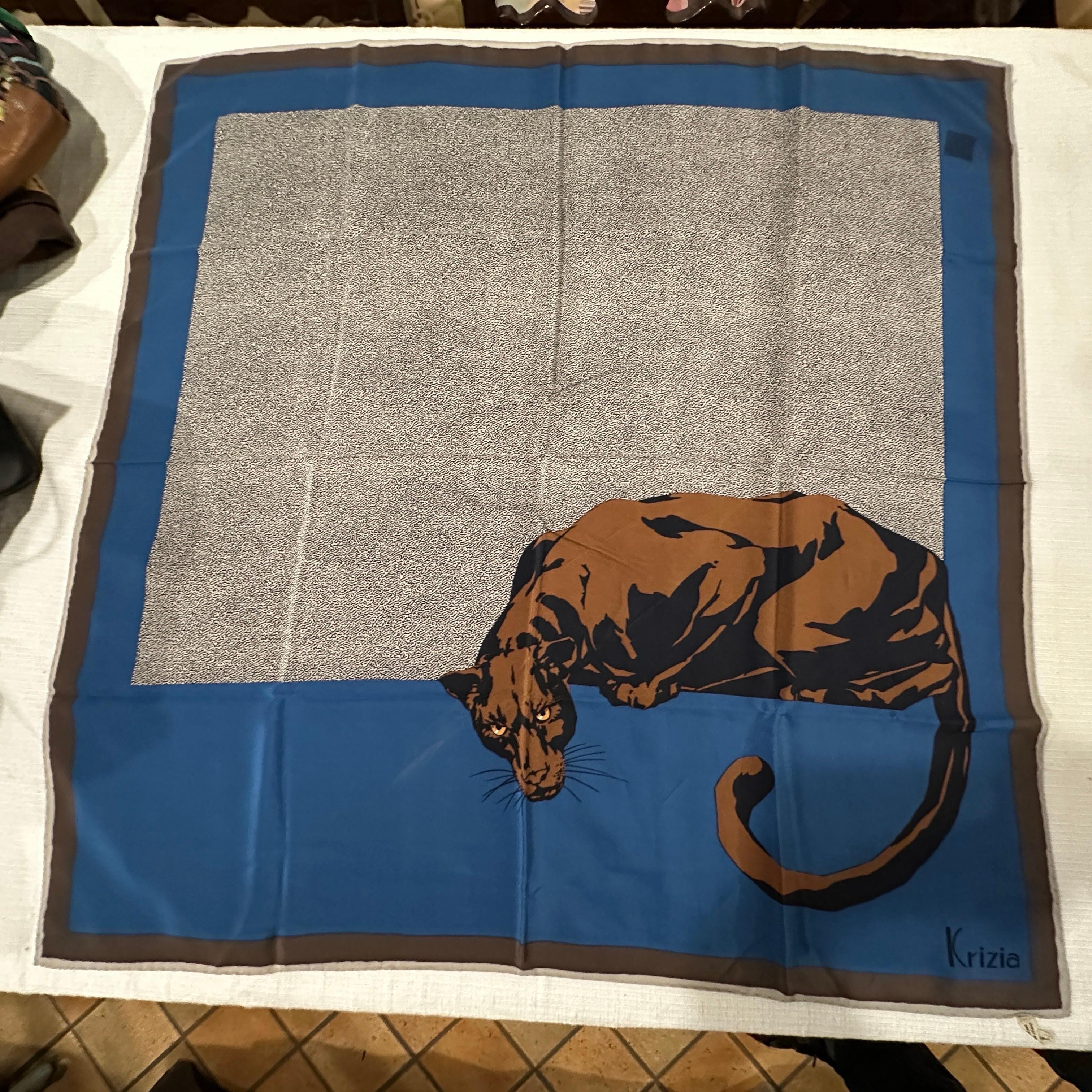 This 1990s silk scarf by Mariuccia Mandelli for Krizia is a striking and artistic accessory featuring a bold panther design. The scarf has a square shape with a rich color palette of blue, brown, and beige. The panther, depicted in a crouching
