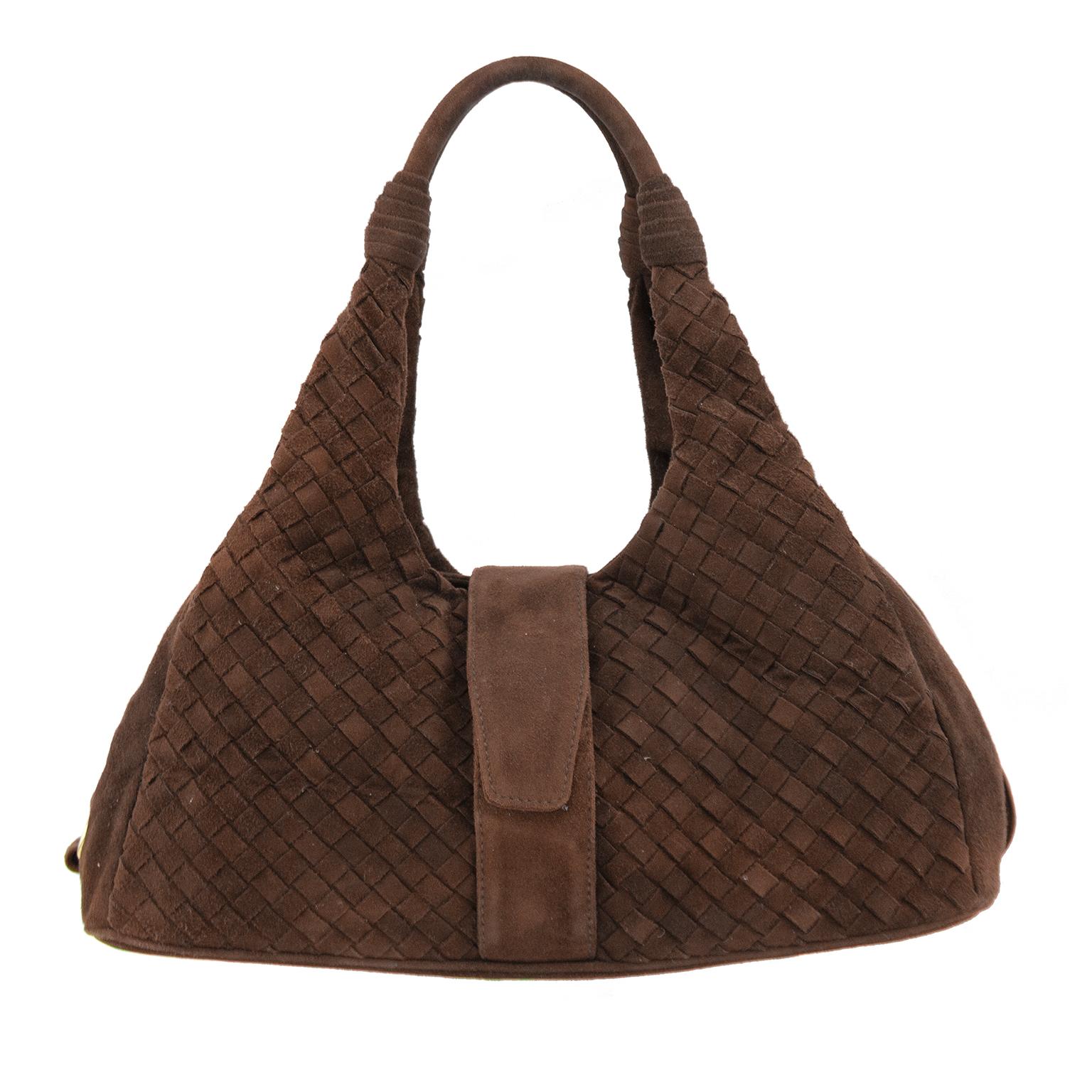 With the popular return of Bottega Veneta, these are the bags everyone wants to get their hands on. Bottega Veneta intrecciato weaved, top handle, hobo style bag. Brown suede with gold hardware. Overlapping belt like straps close bag. Brown suede