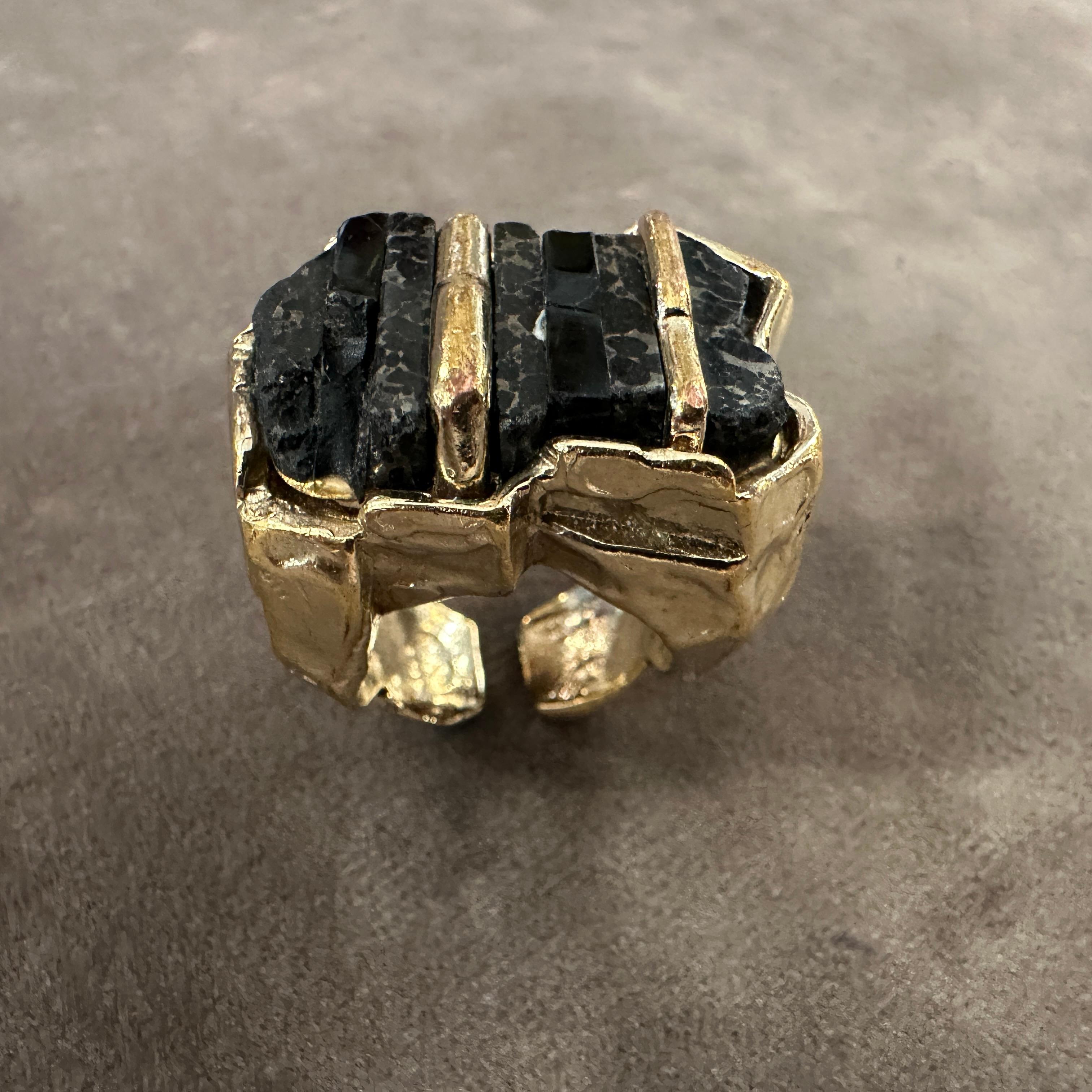Questo audace anello da cocktail anni '90 di Roberto Cavalli è caratterizzato da una sorprendente combinazione di texture e materiali. L'anello è realizzato in ottone scolpito, formando un design unico e artistico. Una pietra nera di grandi