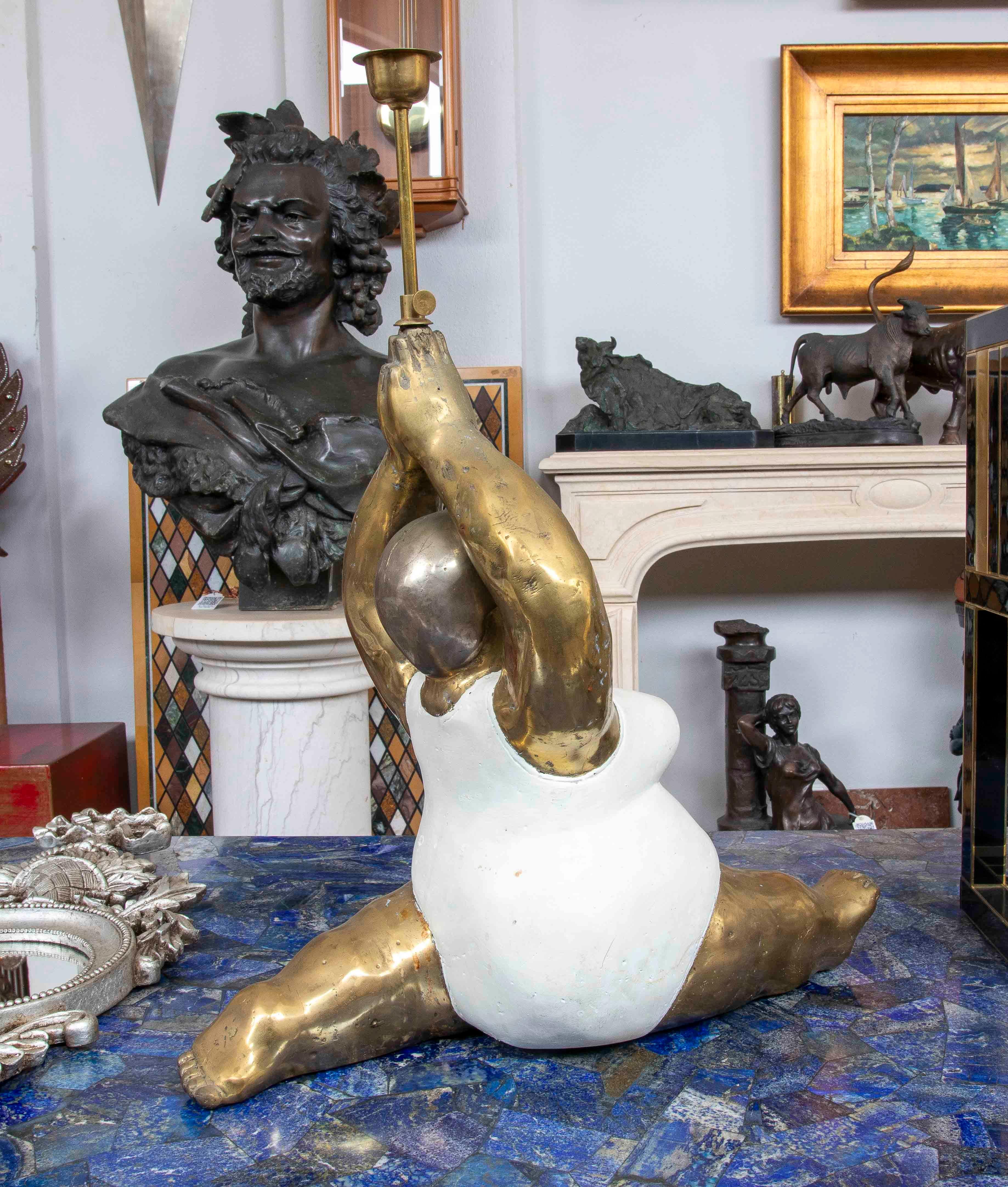 This piece is a decorative sculpture of a dancer in a split position, fusing voluptuous forms with a modern and playful aesthetic. The figure is crafted from polished bronze and white resin, with a robust and expressive body that conveys strength