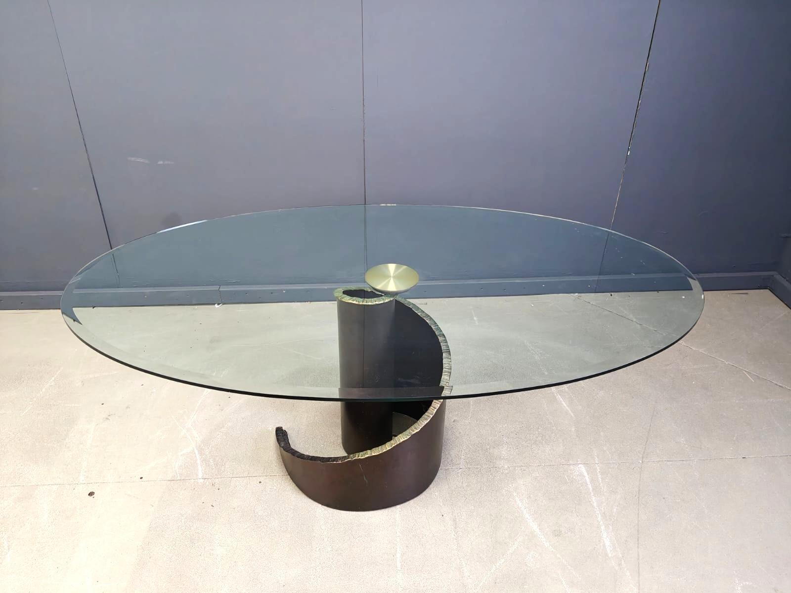 Table de salle à manger de style Brutalist en verre trempé, biseauté et fumé et base en bronze de Maurice Barilone pour Roche Bobois. Le plateau de table ovale en verre des années 1990 repose sur une base en bronze en spirale. Un pad rond en métal