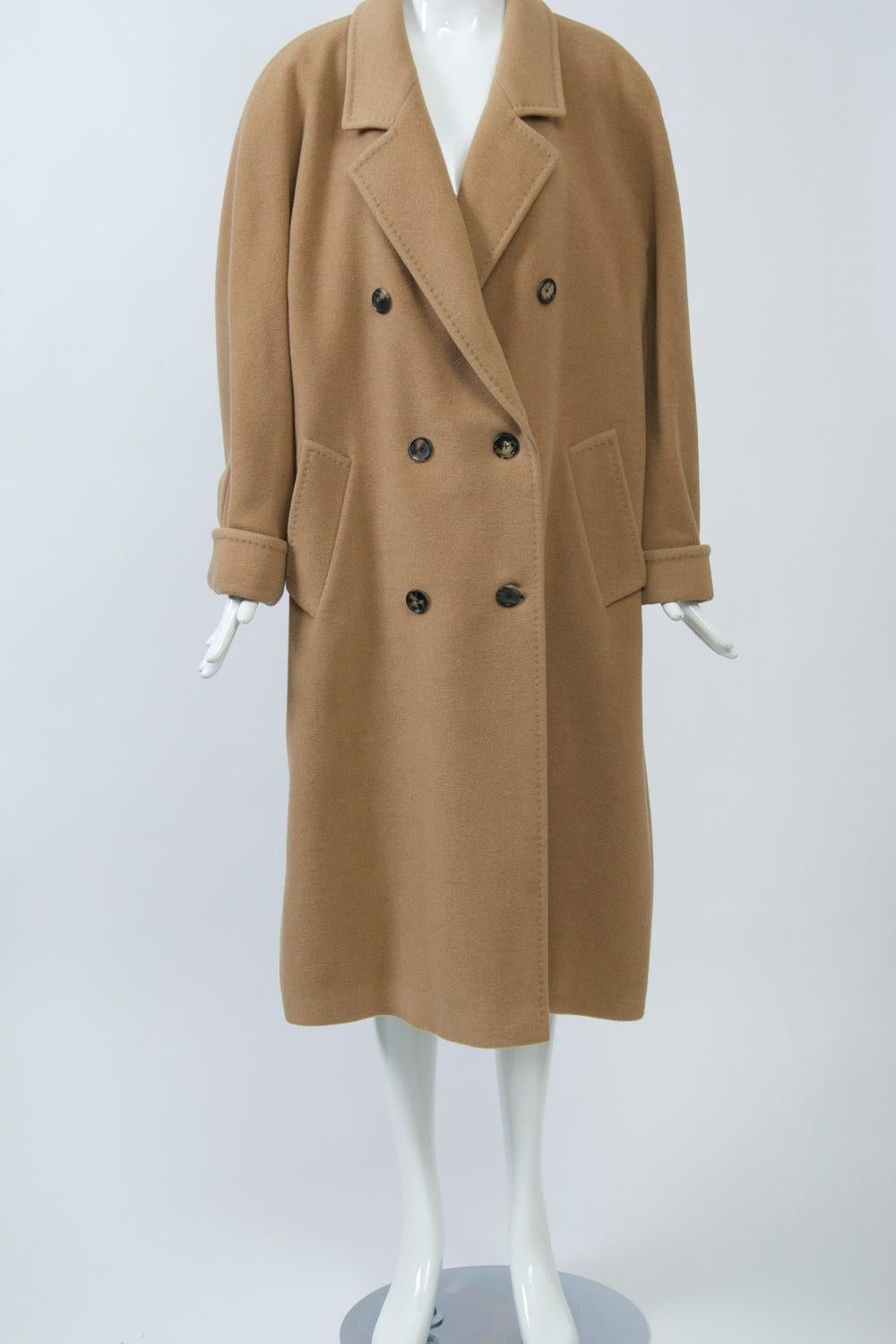 100% camelhair double-breasted coat featuring an oversized fit, notched collar, raglan sleeves with turned back cuffs, and diagonal pockets. Topstitching on seams and edging for a hand finished look. Matching lining. Retailed by well-known German