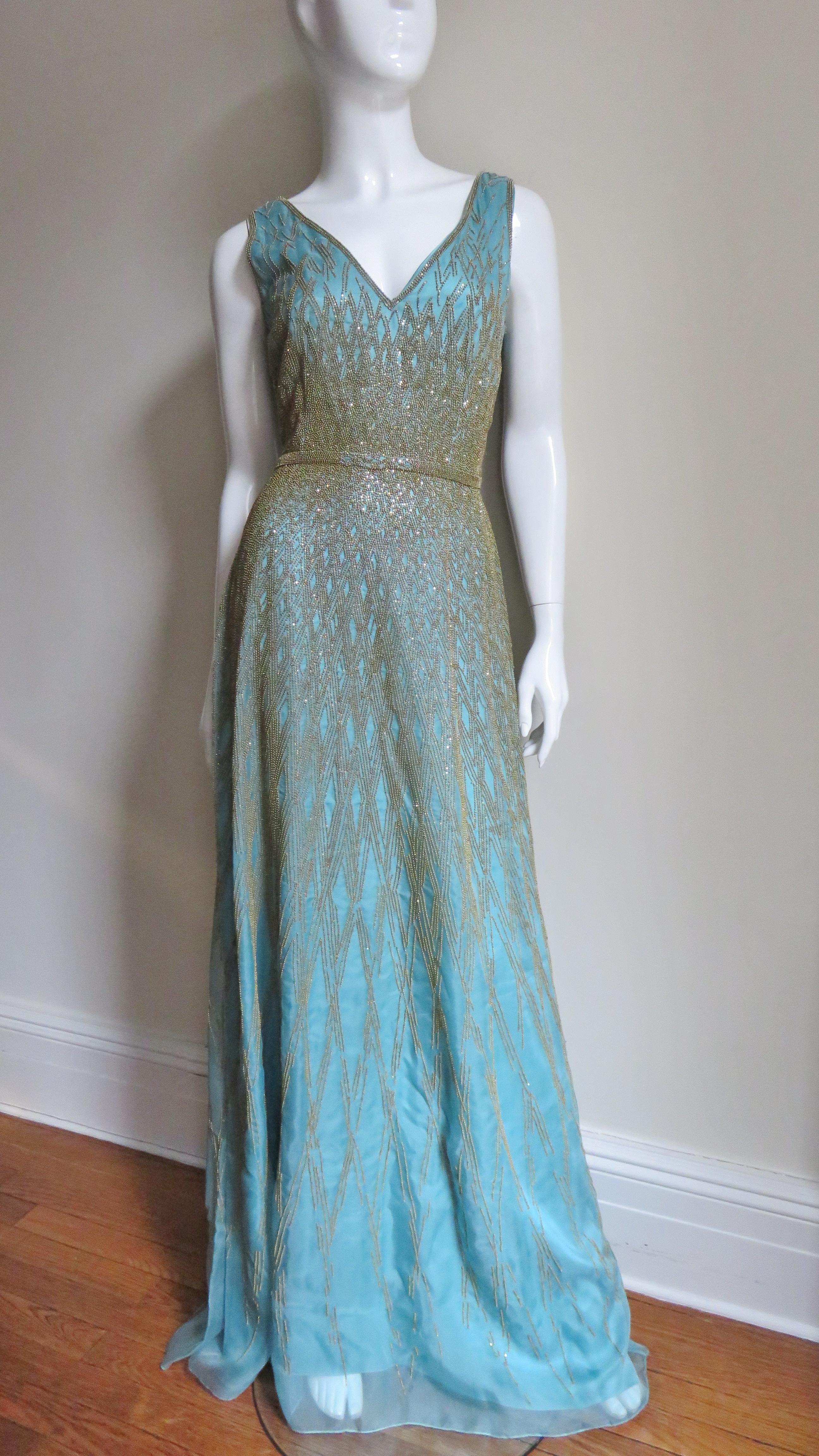 A gorgeous aqua silk gown covered in an elaborate pattern of gold glass beading by Carolina Herrera.  It is sleeveless with a V neckline, fitted waist, and full skirt.  There is an intricate diamond pattern of gold glass beading on semi sheer aqua