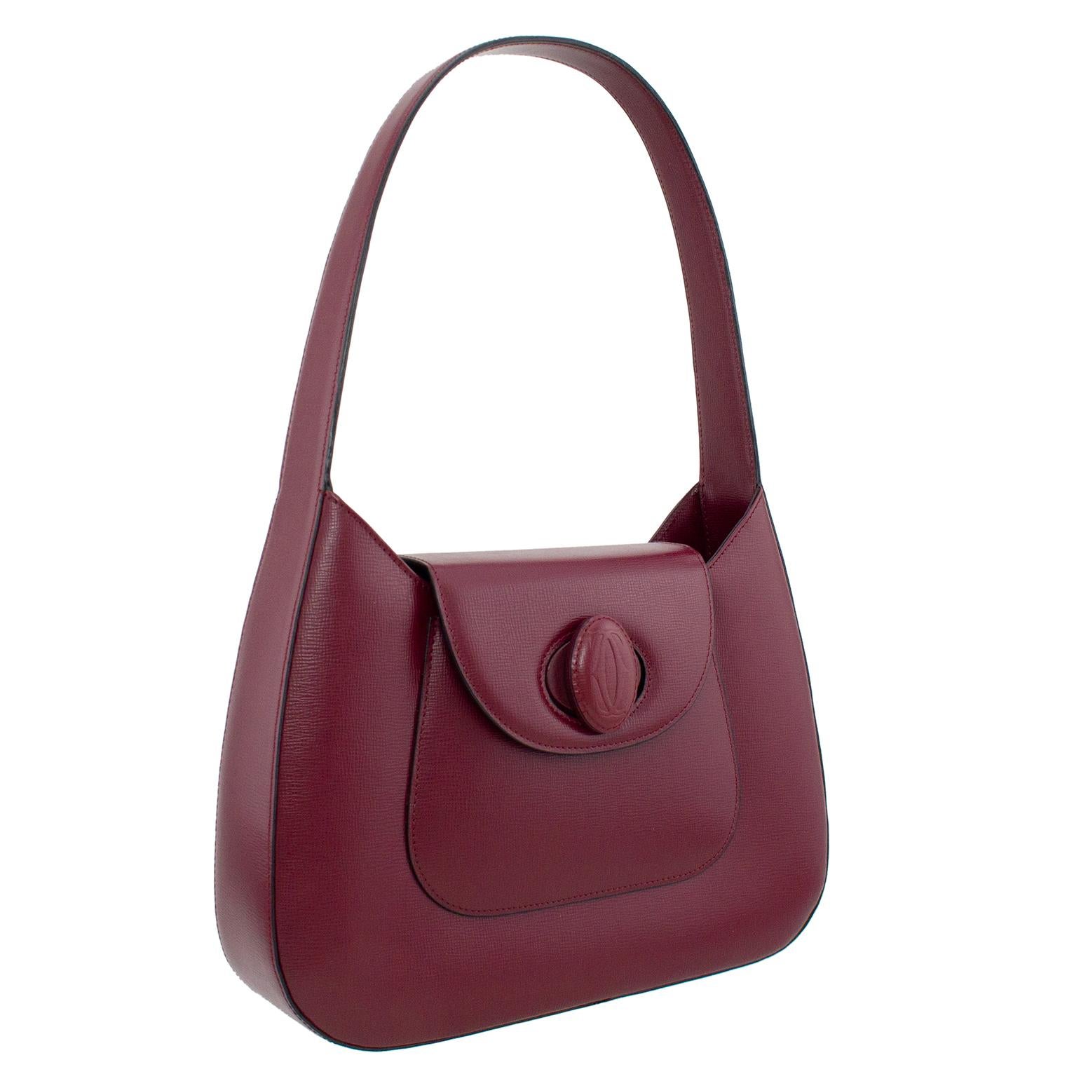 Cartier maroon pebbled leather structured handbag from the 1990s. Long stiff single handle and flap top closure with an oval shaped twist lock. Single slit front exterior pocket. Interior is lined in Maroon Cartier logo fabric with a large