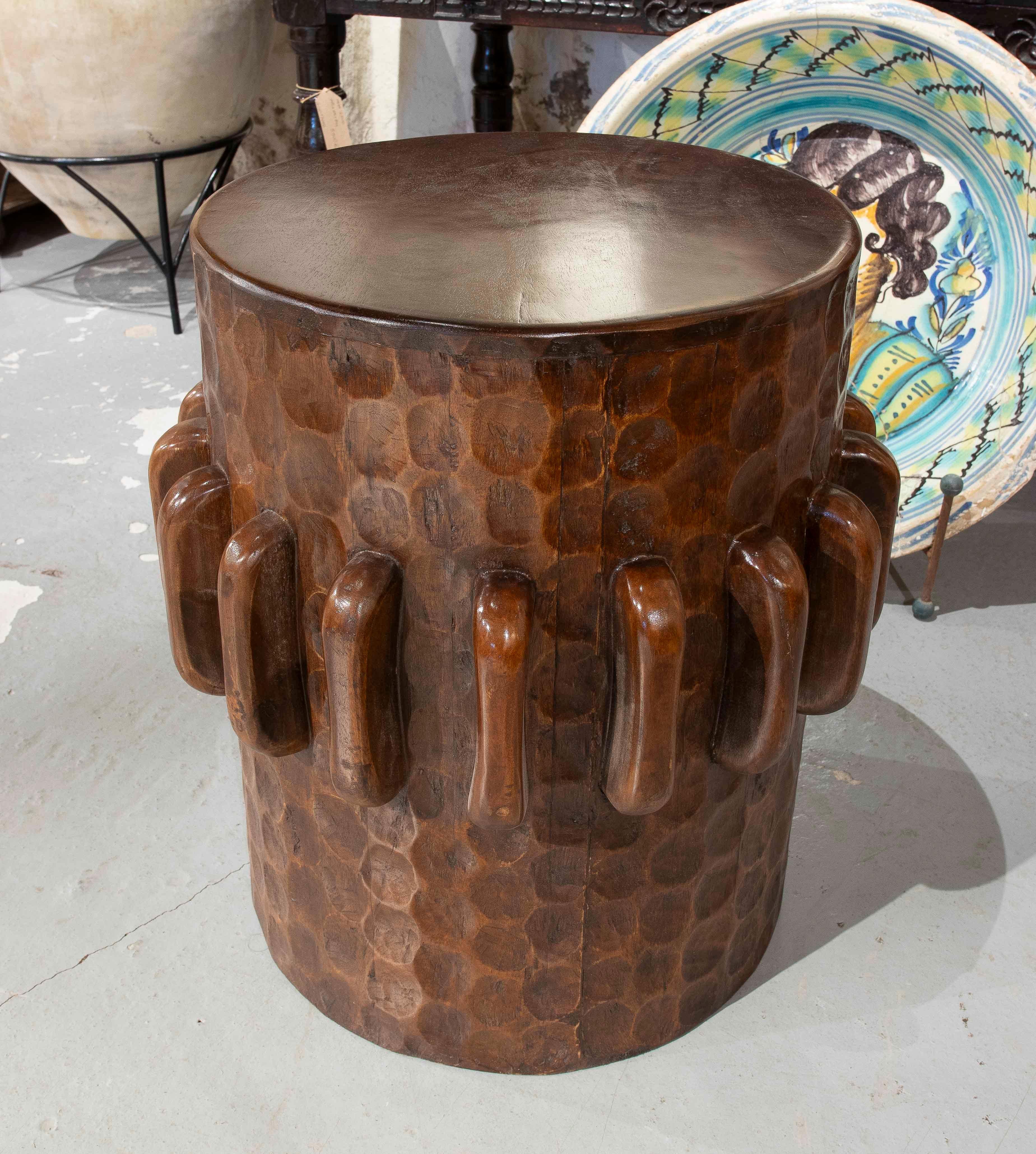 Stunning carved solid wood stool, with a design inspired by ethnic and tribal aesthetics. Its cylindrical structure features a relief of geometric shapes on the surface, providing texture and a unique handcrafted finish.

The curved relief elements