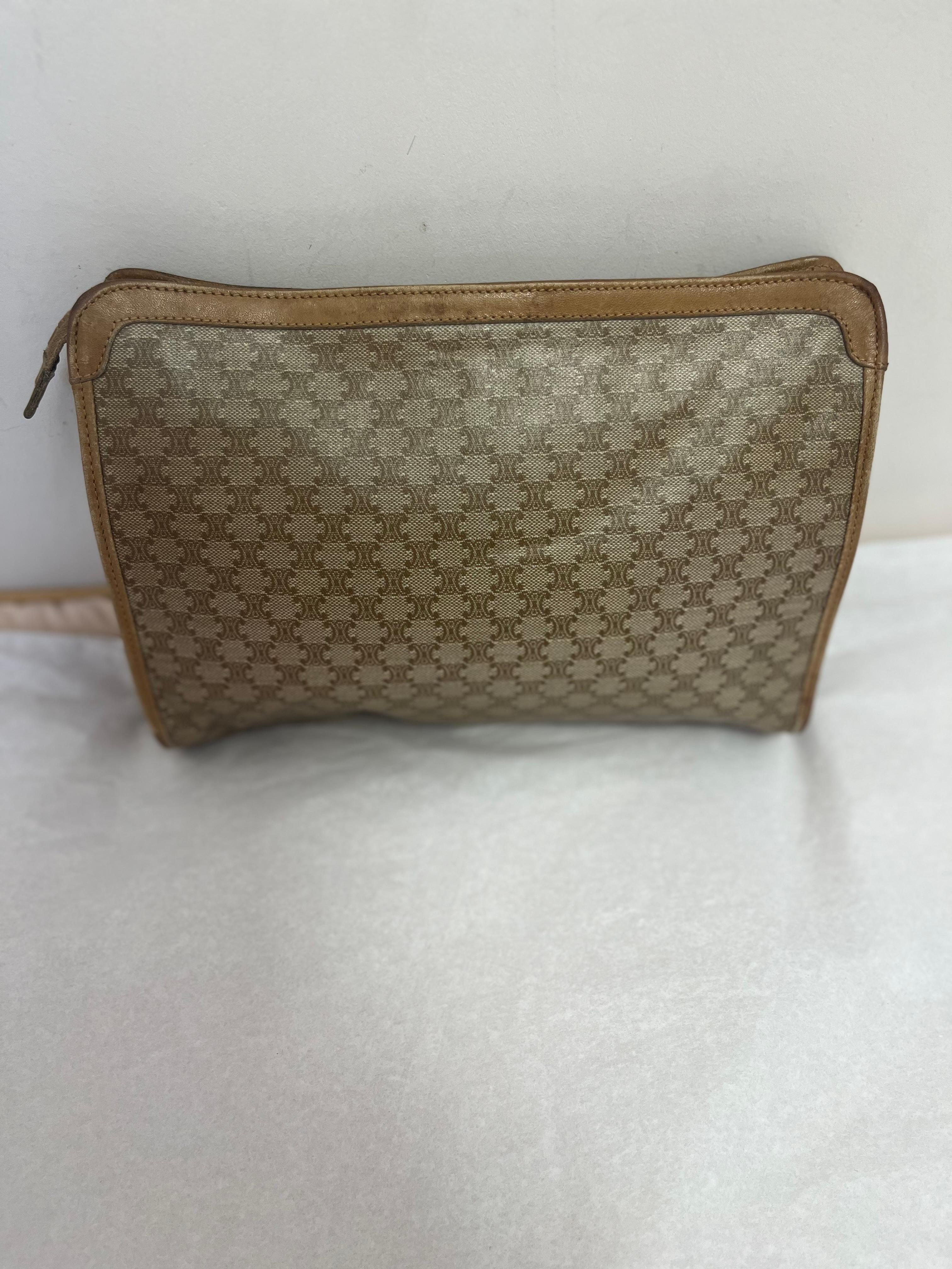 This is a canvas and leather Macadam clutch in brown from the design house of Celine which was established in the 1940s and is still operating today.
The leather lining has a large zipped pocket, and the top zip closure has a Celine stamped