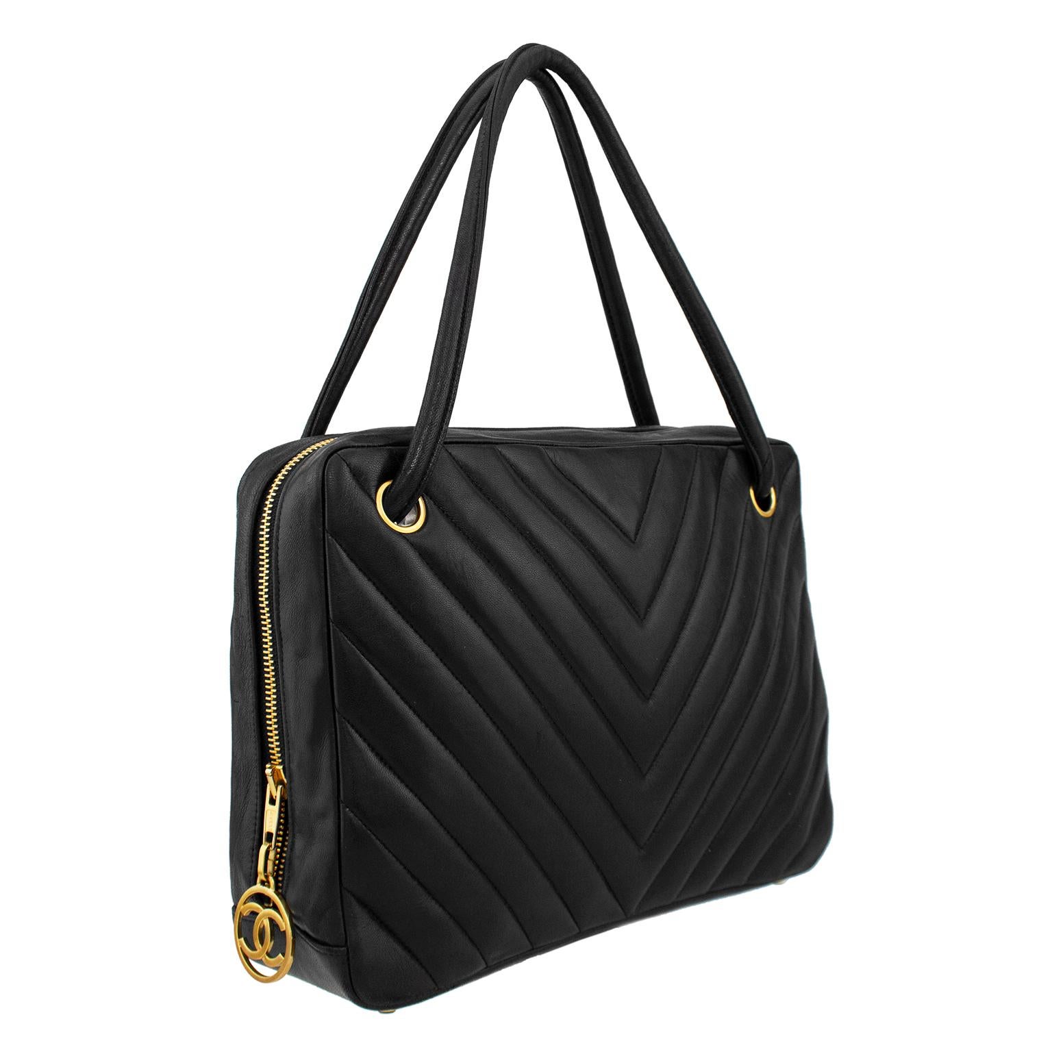 Chanel large camera bag from the 1990s. Supple black lambskin leather in chevron pattern with single exterior slit pocket. Black leather double top handles with are connected in one continuous loop through gold tone metal grommets. Gold tone metal