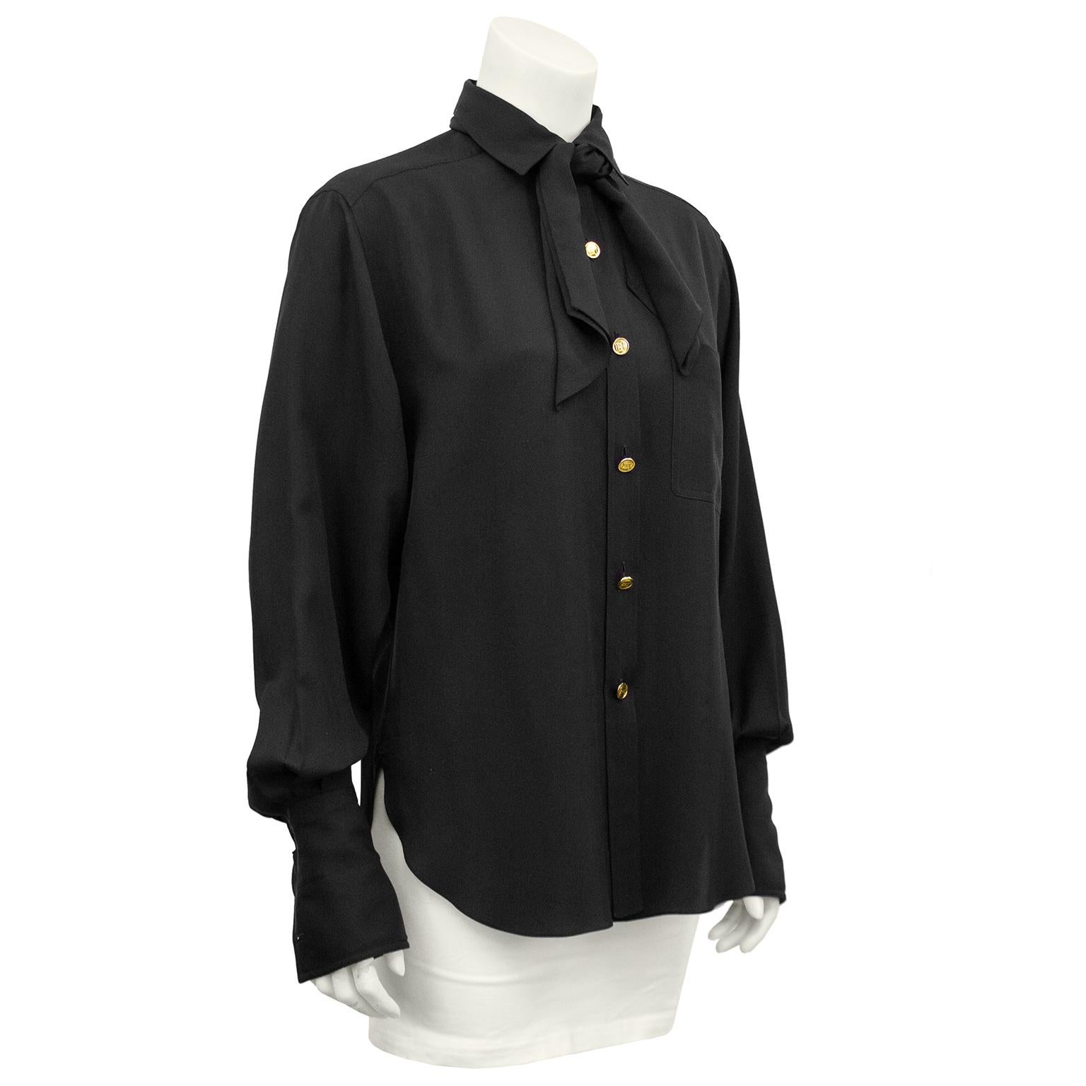 The quintessentially perfect Chanel 1990s blouse. Black silk and slightly oversized throughout the body with a tie at the neck. Bishop sleeves with oversized cuffs that extend over the hands. Bright gold, amazing Chanel buttons engraved with the