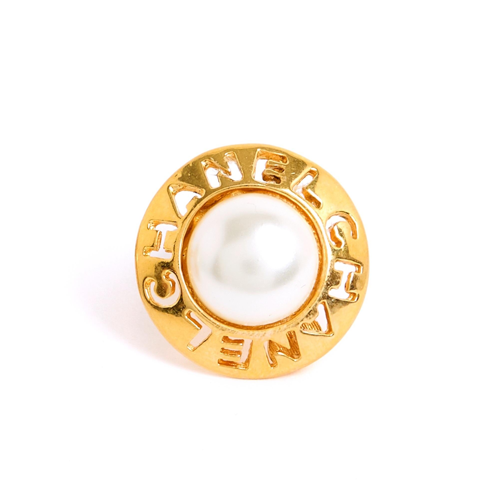 Chanel-Ohrringe, goldene Metallklammern mit durchbrochenen Buchstaben CHANEL, in der Mitte eine halbe ecrufarbene Zierperle, um 1990. Durchmesser 2.5 cm. Die Ohrringe weisen leichte Altersspuren auf, sind aber in sehr gutem Zustand, Sammlerstück und