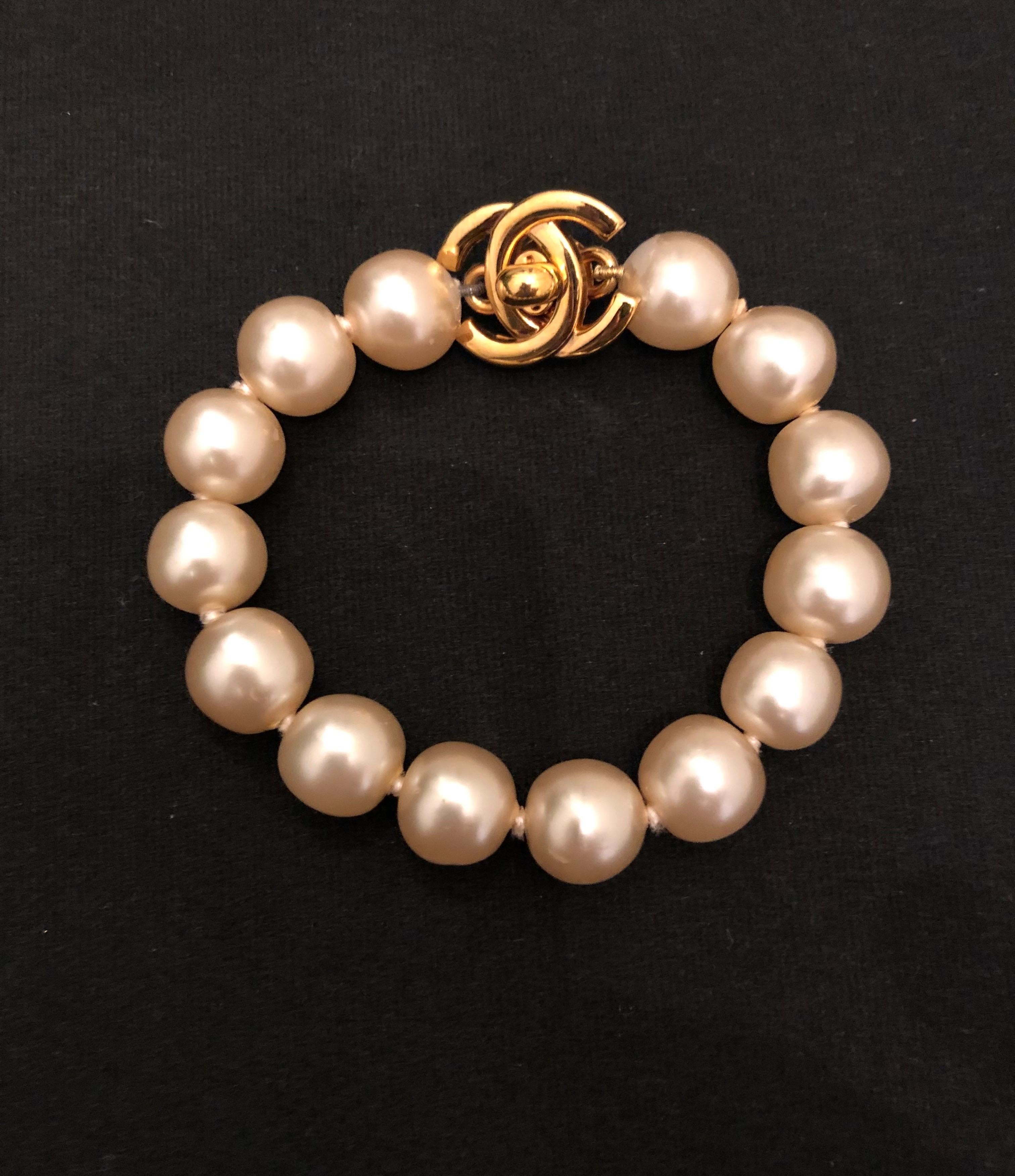 1990s Chanel faux pearl bracelet featuring an iconic Chanel turnlock in gold toned metal. Stamped Chanel 96P made in France. Turn lock closure. Inner circumference measures approximately 16 cm faux pearl 1.2 cm Turn lock 2.1 x 1.7 cm. Comes with