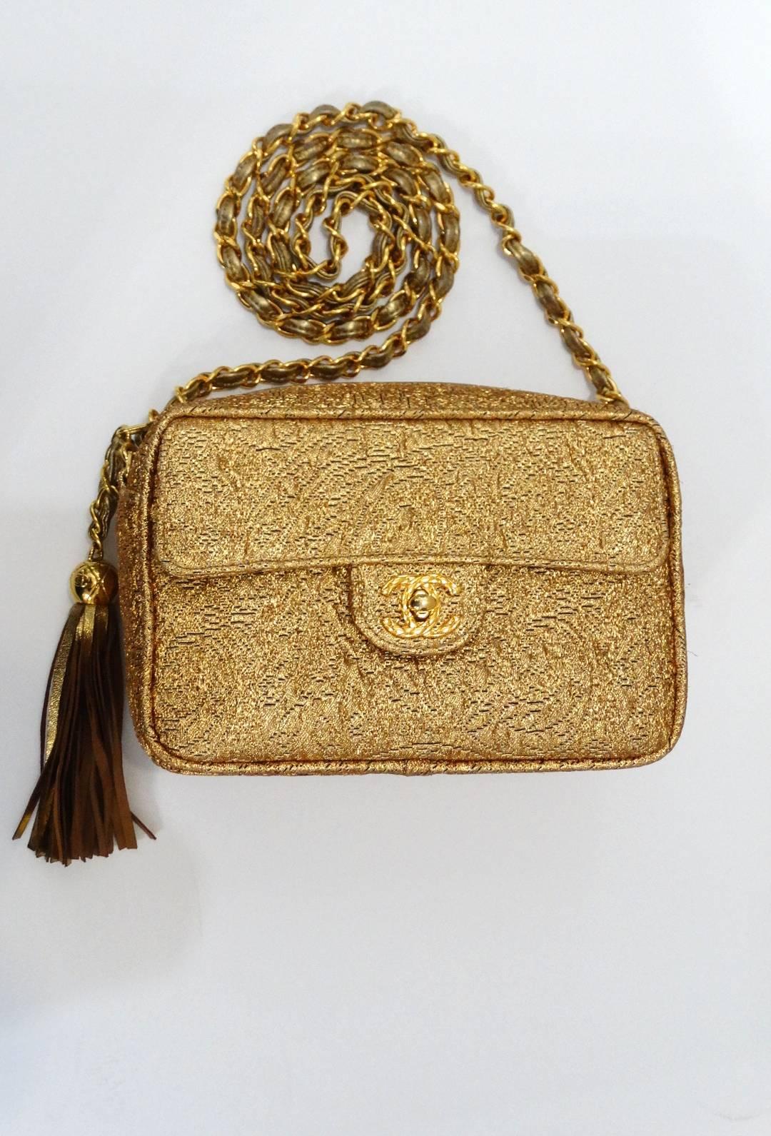 Treat yourself with our gorgeous 1990s Chanel brocade camera bag! Made of a unique embossed gold leather in an intricate brocade pattern. This bag has the classic gold metal chain with leather woven throughout. Zips across the top with long CC