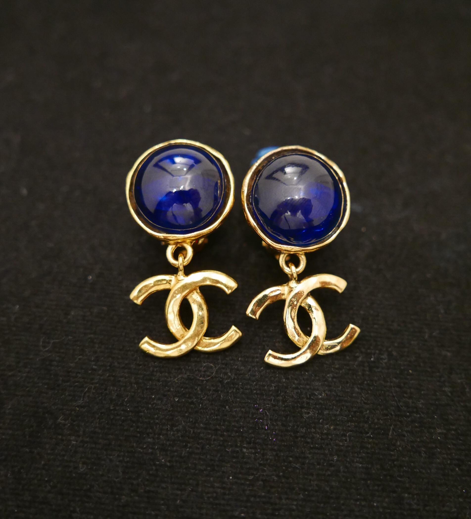 Pair of 1990s Chanel gold toned earclips featuring a blue gripoix hemisphere adorned with a dangle gold toned CC logo. Measures approximately 4.4 x 2.2cm. Stamped Chanel 94P, made in France. Clip on style. Comes with box.

Condition: Minor signs of