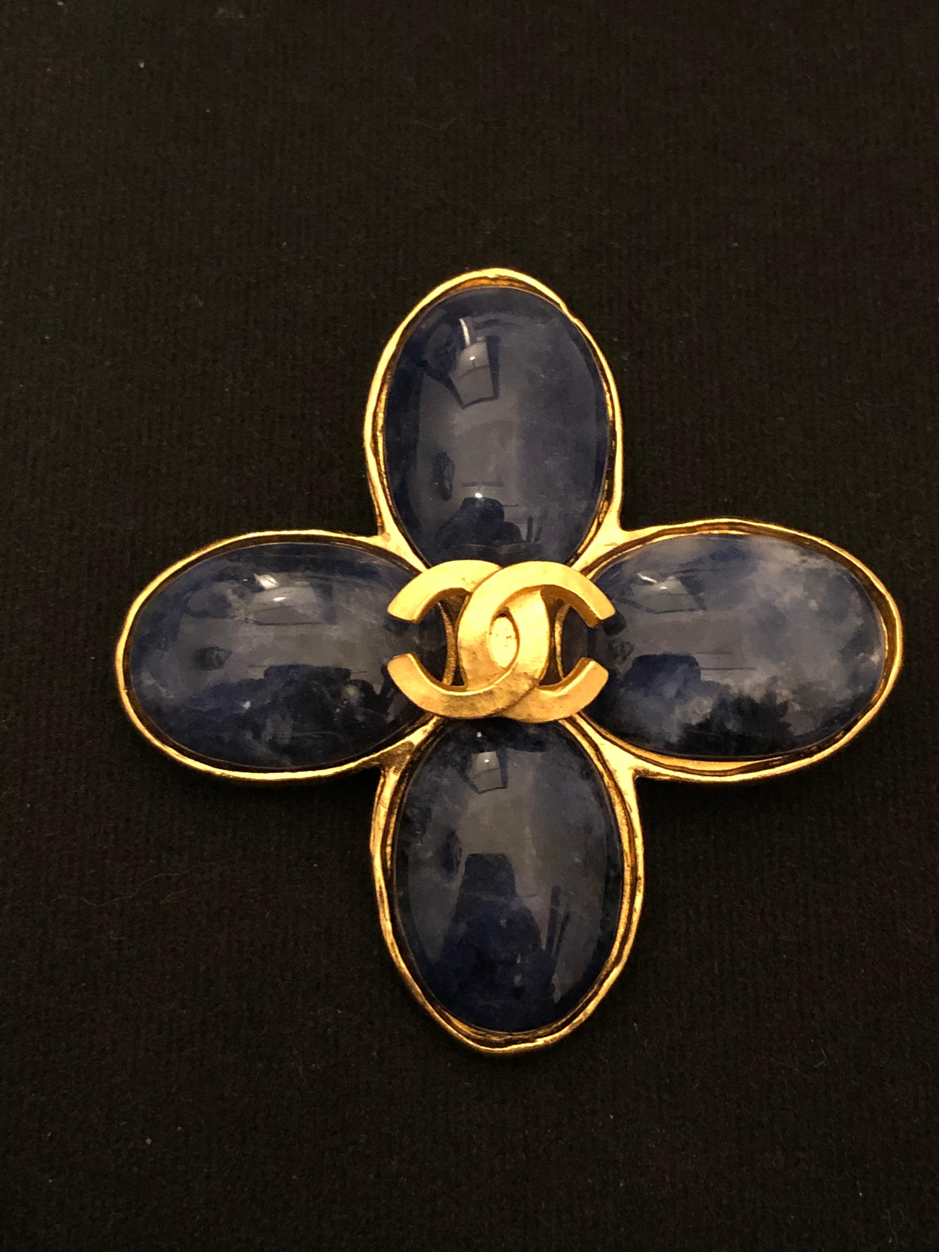 1990s Chanel gold toned clover brooch featuring four CC clover leaves in Lapis Lazuli stone adorned with a gold toned CC at the center. Stamped 95A made in France. Measures approximately 6.2 x 6.2 cm. Comes with box. 

Condition: Minor signs of