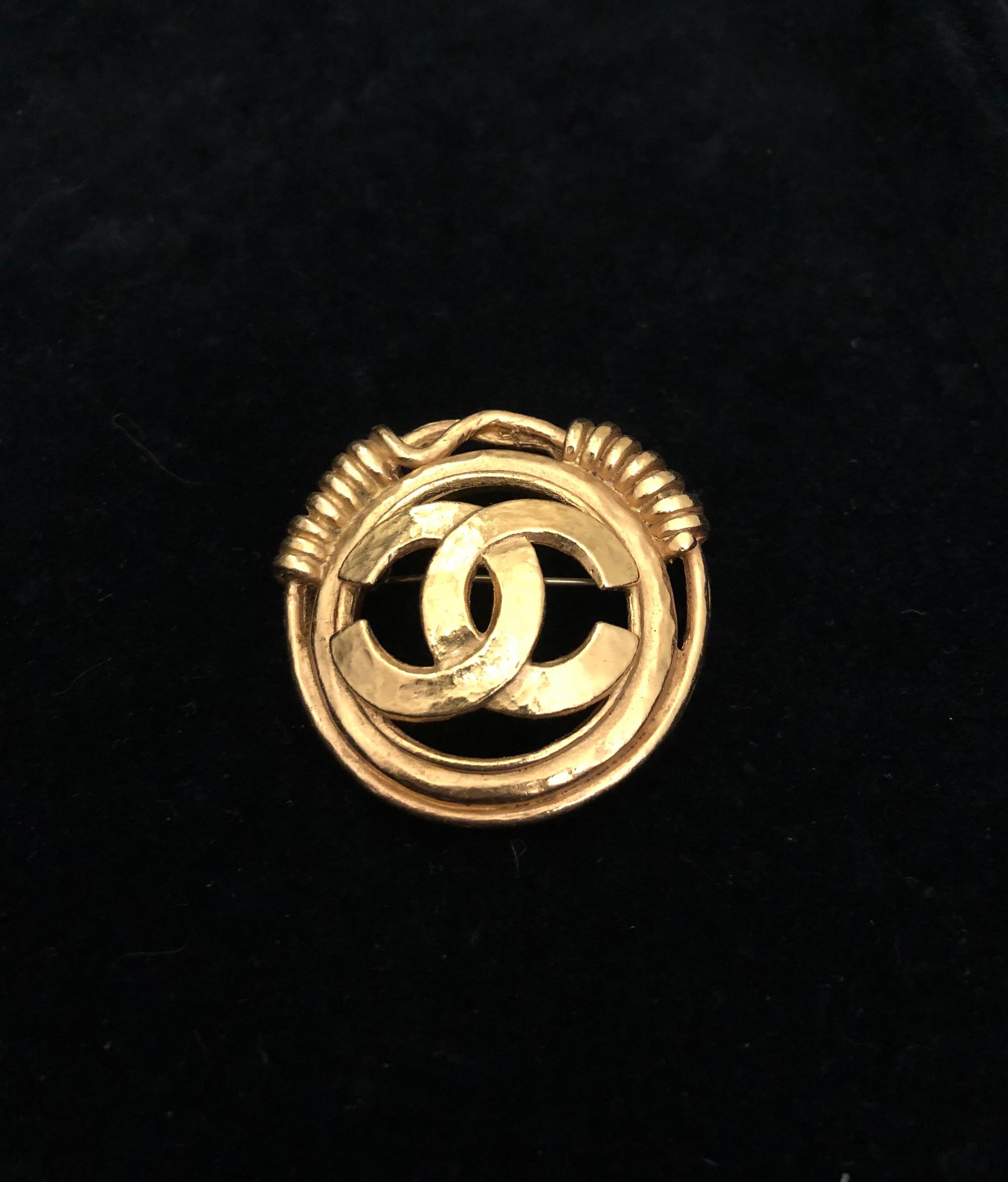1990s Chanel gold toned brooch featuring a CC logo surrounded by a gold toned coiled ring. Stamped 94P made in France. Measures approximately 4.3 cm in diameter. Comes with box. 

Condition: Minor signs of wear. Generally in very good condition.