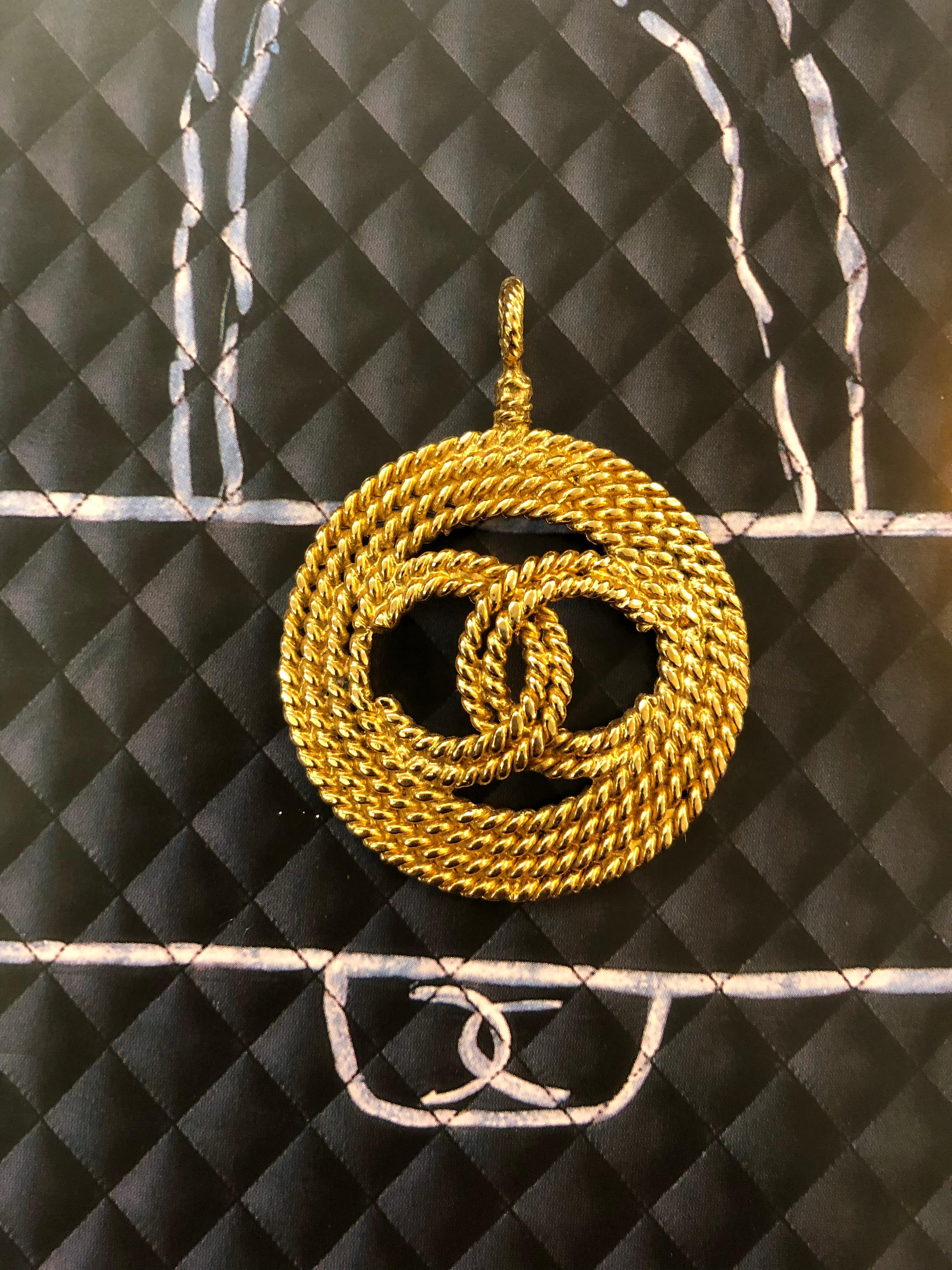 1990s Chanel pendant featuring a gold toned CC surrounded by triple gold toned metal in rope pattern. Stamped Chanel 28 made in France. Measures 4.9 x 6.4 cm. This charm can be secured onto a pearl necklace as shown in the picture.

NOTE: The pearl