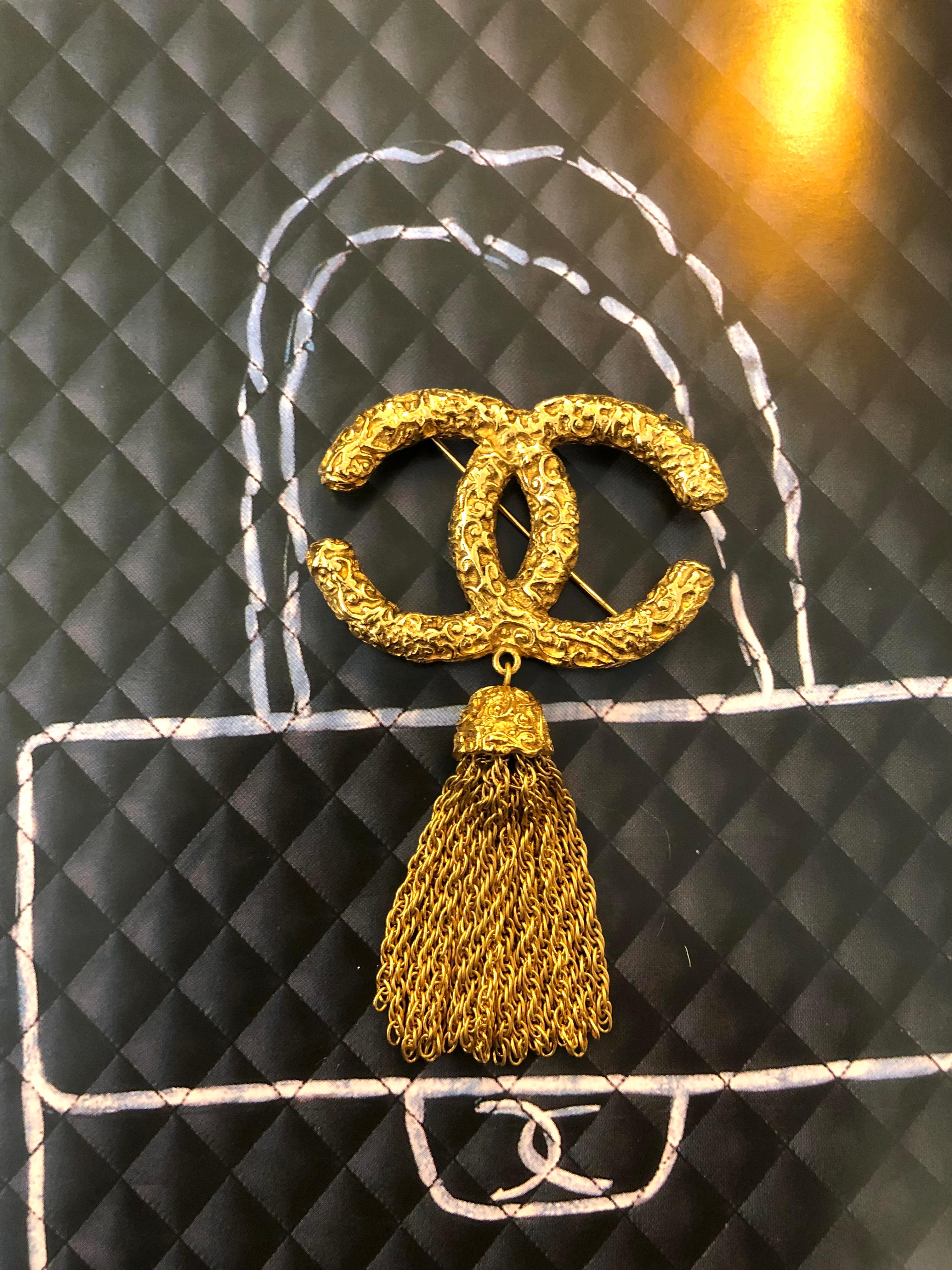 1990s Chanel gold toned brooch featuring a huge CC logo with carved details and a chain tassel.   Stamped 93A made in France. Measures approximately 8.7 x 5.2 cm. Comes with box. 

Condition: Minimal signs of wear. Excellent 
