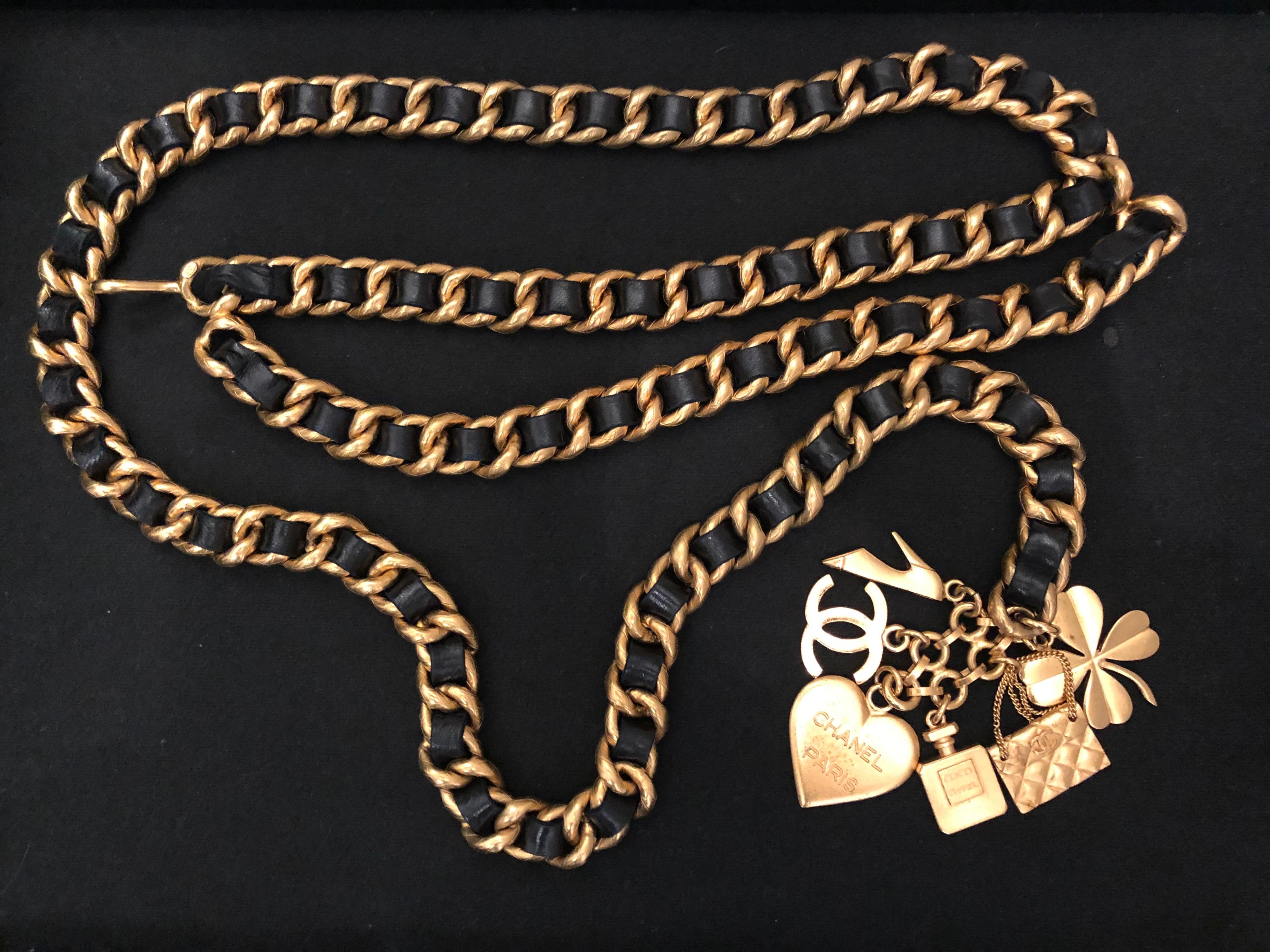 1990s Chanel gold toned chain belt interlaced with black leather featuring six iconic Chanel charms. Stamped Chanel 95A made in France. Adjustable hook fastening. Measures 101 cm in wearable length (excl. charm) chain 1.5 cm in width. Comes with