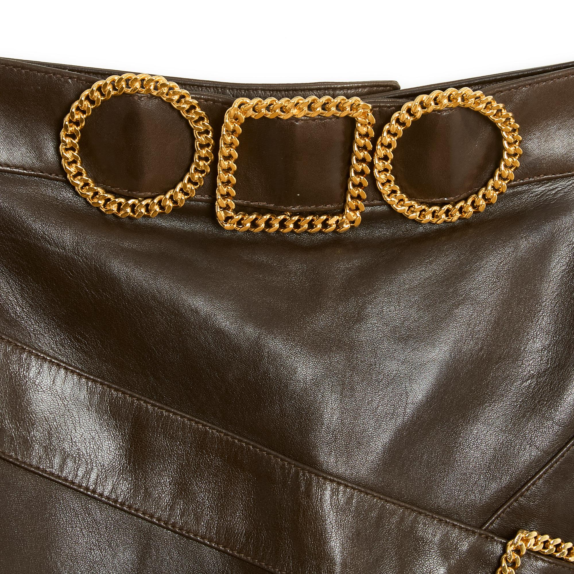 Chanel circa 1990 straight skirt in ultra soft dark brown leather with striped leather inserts decorated with gold metal chain belt buckles, matching CC logo silk lining, zip and button closure in the back. No more size label but the measurements