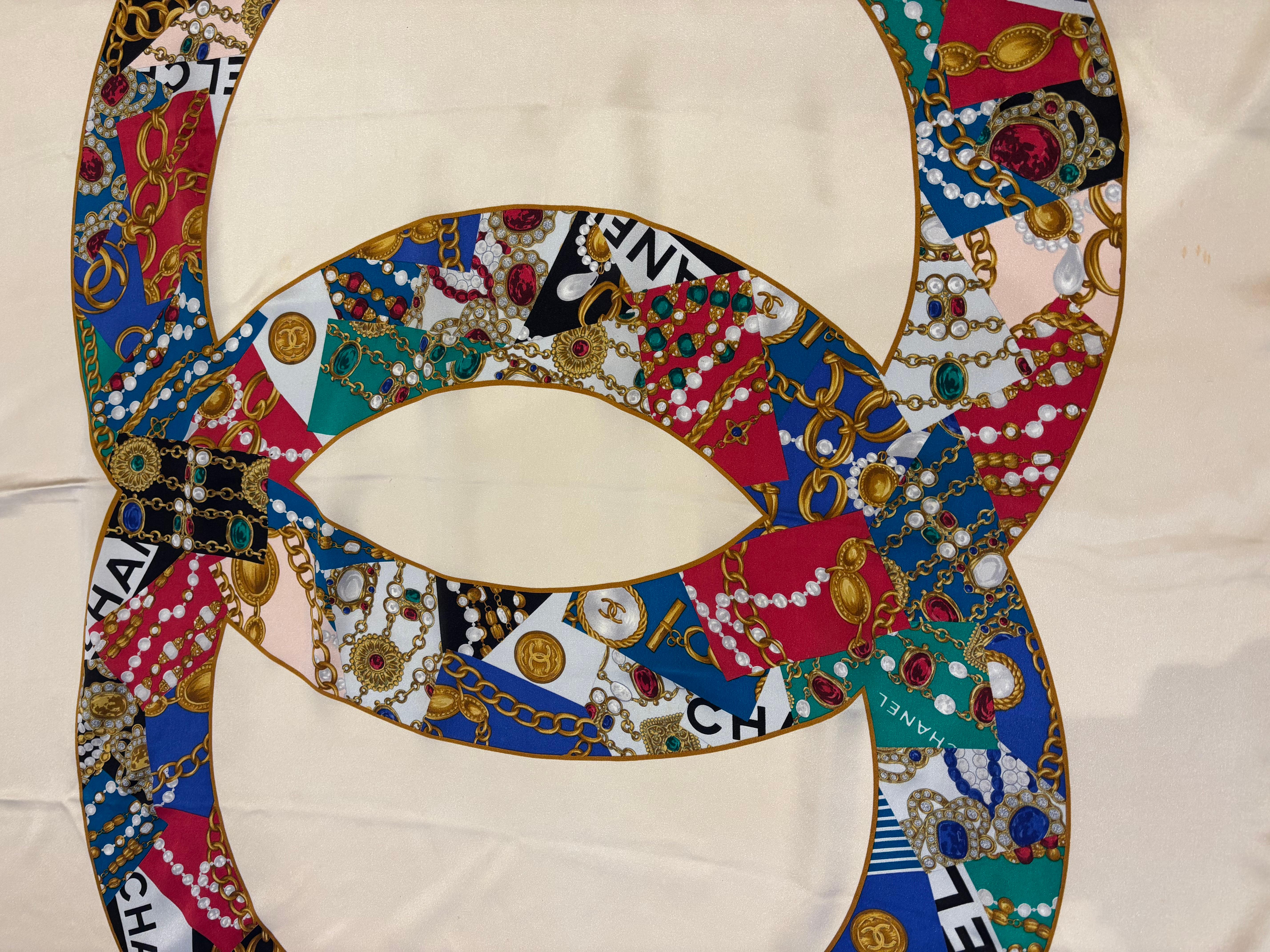 Schöner, ikonischer Vintage-Seidenschal von Chanel aus den 1990er Jahren mit CCs in Gripois-Juwelen.
Der Hintergrund ist cremefarben, in der Mitte des Schals befindet sich ein mehrfarbiges, mit Juwelen besetztes CC, das von den CHANEL-Initialen