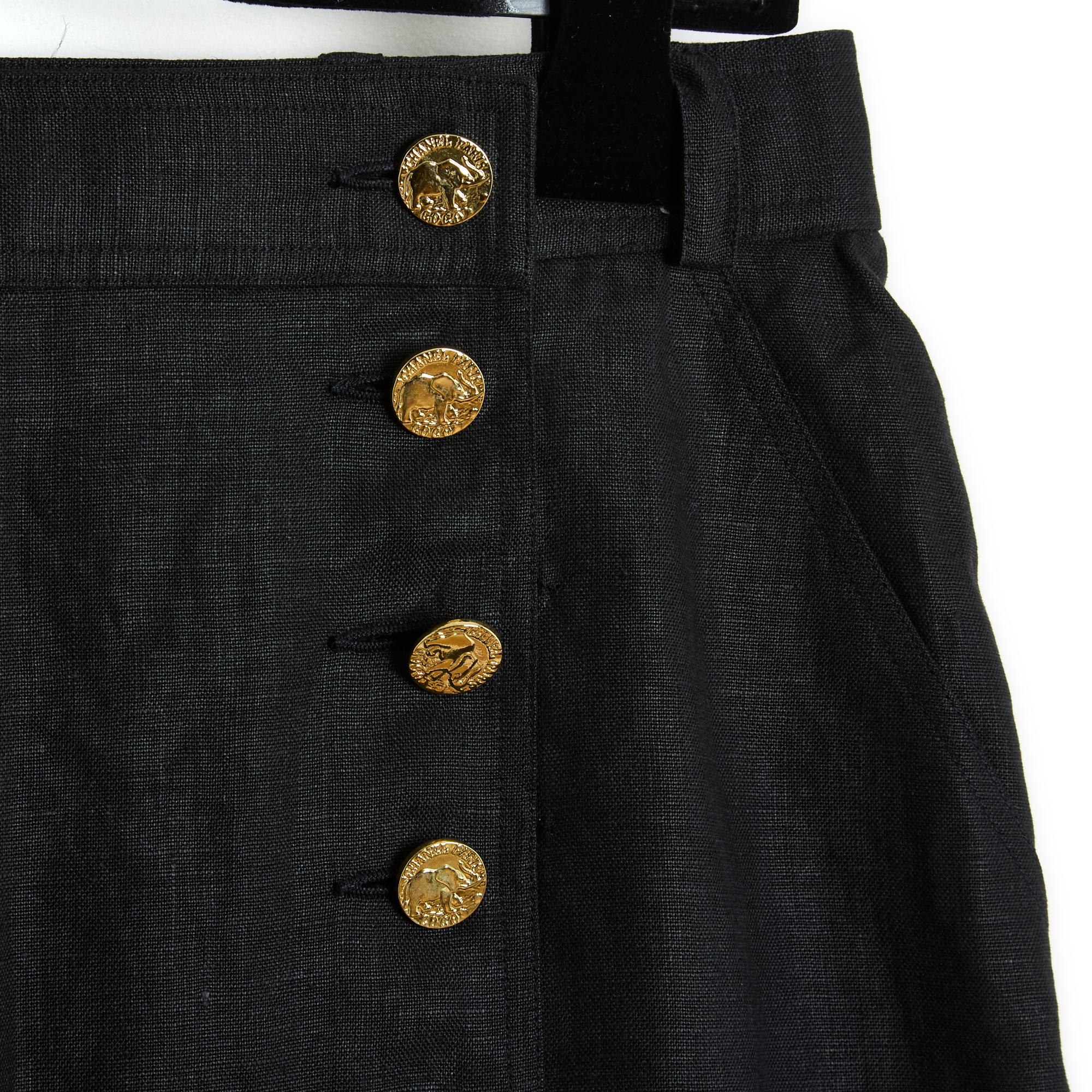 Chanel skirt by Karl Lagerfeld circa 1990 wrap-around style in black linen enhanced with Chanel logo buttons in gold metal, 2 slanted slit pockets, belt loops, silk lining. No more size label but the measurements indicate a 40/42FR or 10/12US: waist