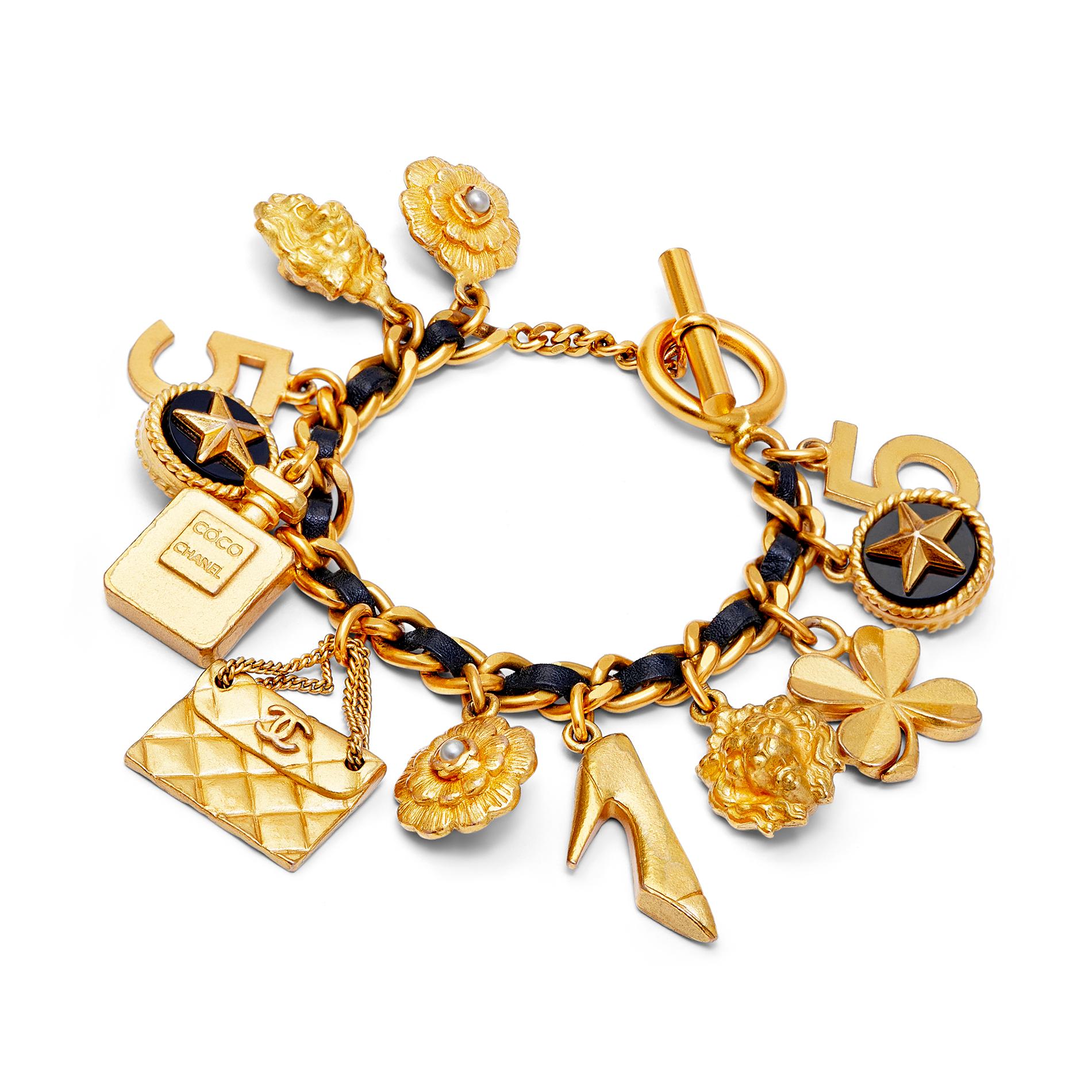 1990s Chanel gold-toned metal and black leather bracelet with the House's famous charms including: camellia flower with pearl centre, classic quilted handbag, monochrome court shoe, perfume bottle, 4-leaf clover, lion head, 5-point star and iconic