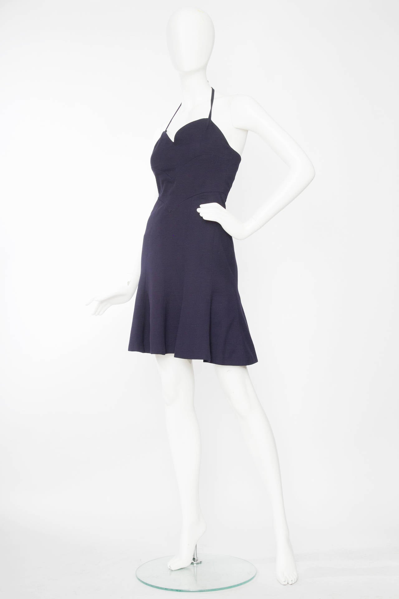 A flirty 1990s Chanel Boutique navy blue cotton dress with an adjustable strap halter-neck, The dress has a low cut front and a ruffle hemline. The dress closes in the back with a zipper closure. 

The size of the dress corresponds to a modern size