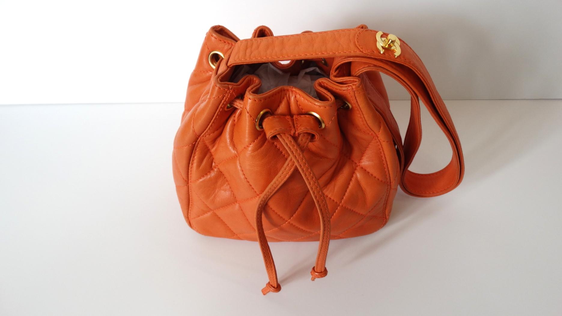 Treat yourself to a piece of fashion history- Karl Lagerfeld era Chanel orange bucket bag circa 1994-1996! Crafted from a soft lambskin leather and stitched with Chanel's signature quilting. Bucket-bag style construction with leather shoulder strap.