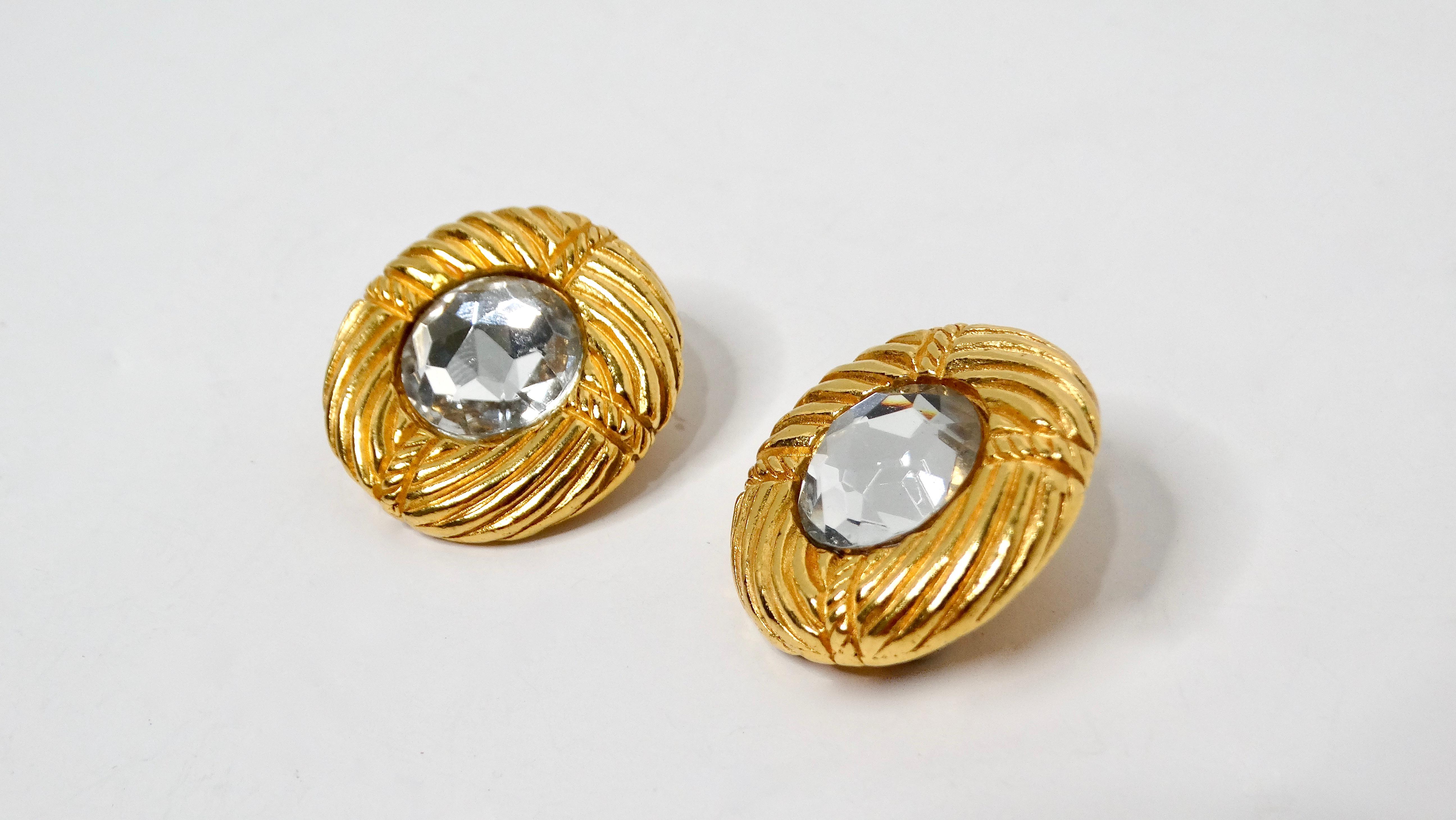 Eleva il tuo gioco di accessori con questi splendidi orecchini a clip con strass tondi e nervati di Chanel degli anni '90. Caratterizzati da un accattivante strass di grandi dimensioni al centro di un cerchio rotondo a coste in tonalità oro, questi