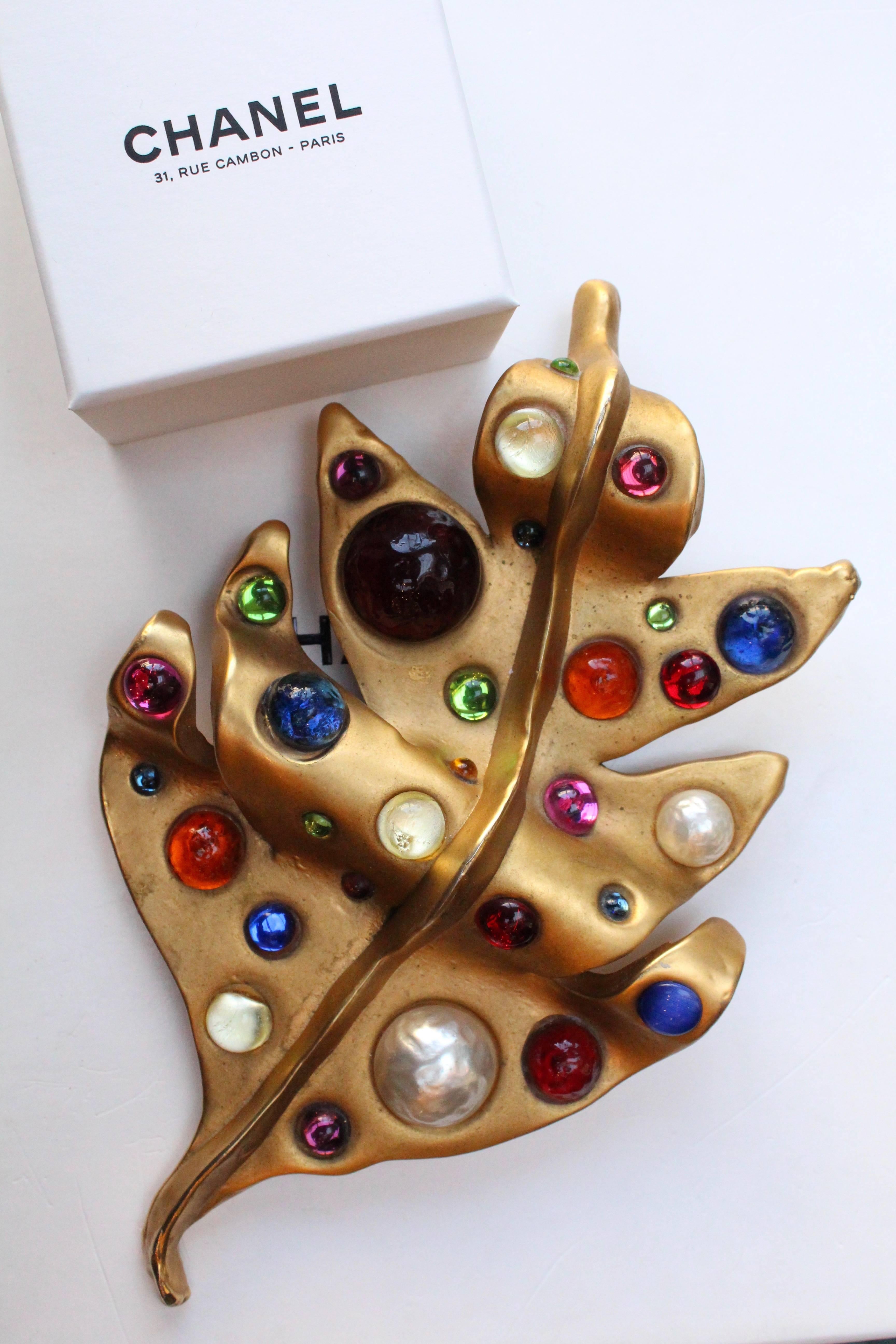 CHANEL (Made in France) Rare one-of-a-kind gilded metal brooch representing an undulating leaf. It is decorated with multiple round glass paste cabochons in sapphire, ruby, amber, emerald, amethyst, pink colors and translucent and pearly cabochons.