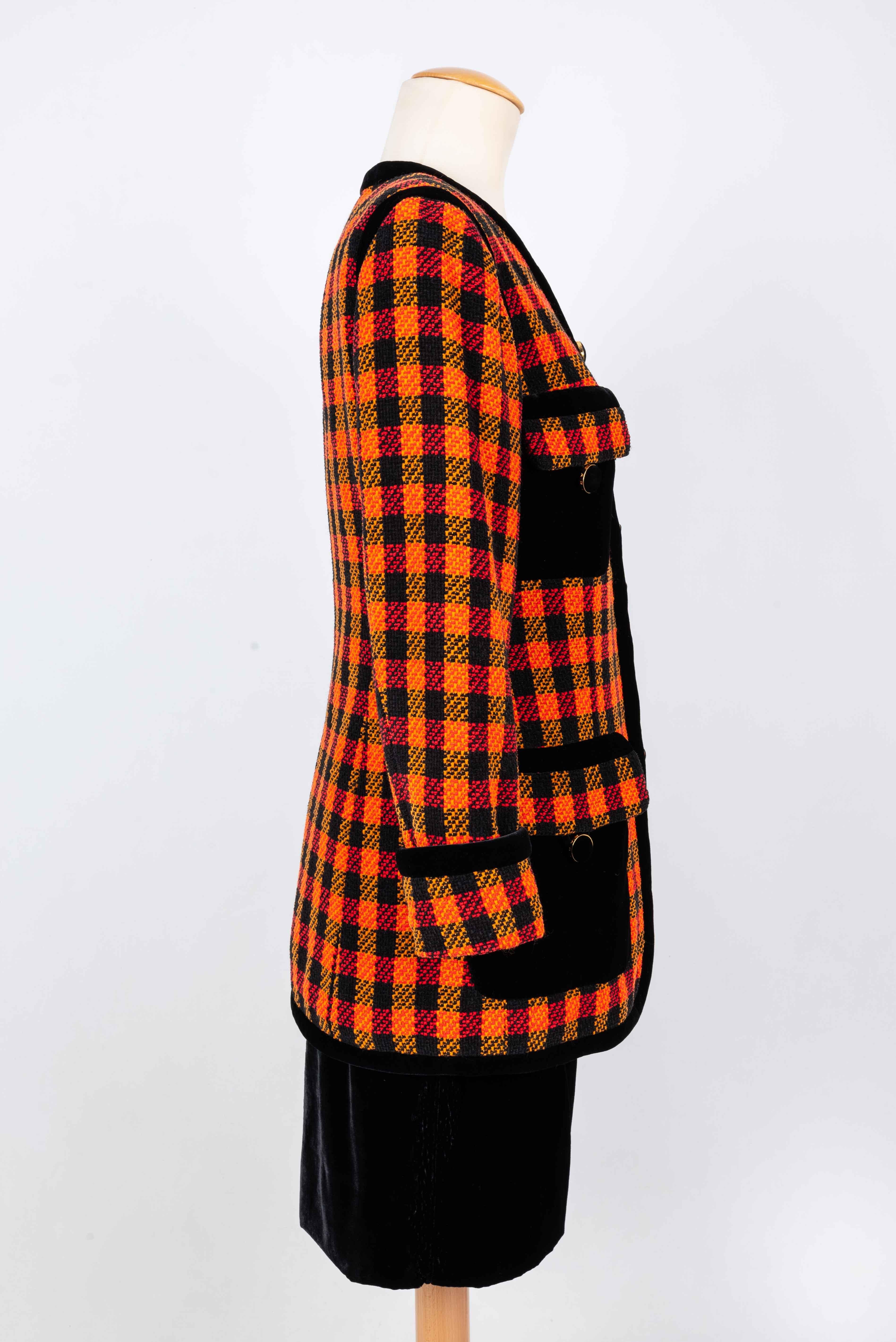 CHANEL (Made in France) Suit consisting of a skirt and a jacket in tweed check in shades of yellow, orange and red. The pockets and the turn of the jacket are in black velvet. 
Silk lining. 
Size shown 38FR.
This outfit dates from the 1990s. 
