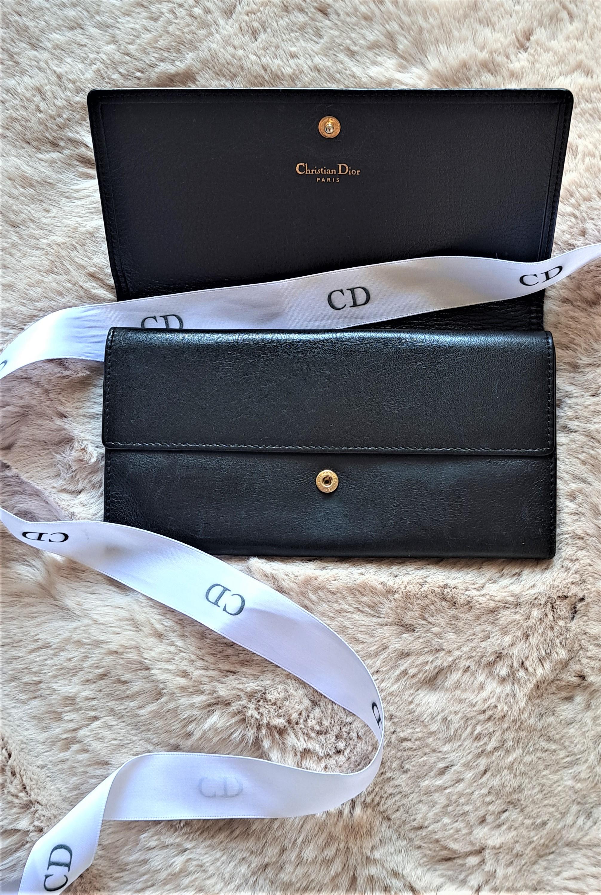 Dieses wunderschöne schwarze Portemonnaie aus Kalbsleder von Christian Dior aus den 1990er Jahren mit goldenem Charme-Logo ist ein klassisches und ikonisches Accessoire. 

In den 1990er Jahren erlebte Dior einen erneuten Popularitätsschub, und die