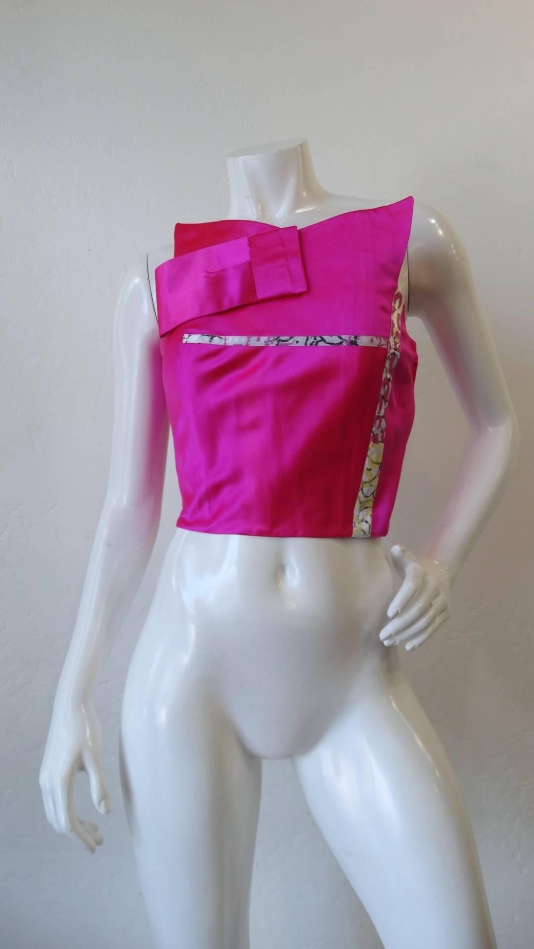 The most incredible 1990s bustier top from iconic designer Christian La Croix! Unique origami inspired silhouette with high neckline and sleeveless fit. Made of a bold hot pink silk fabric with hints of printed trim up the bodice. Zips up the side.