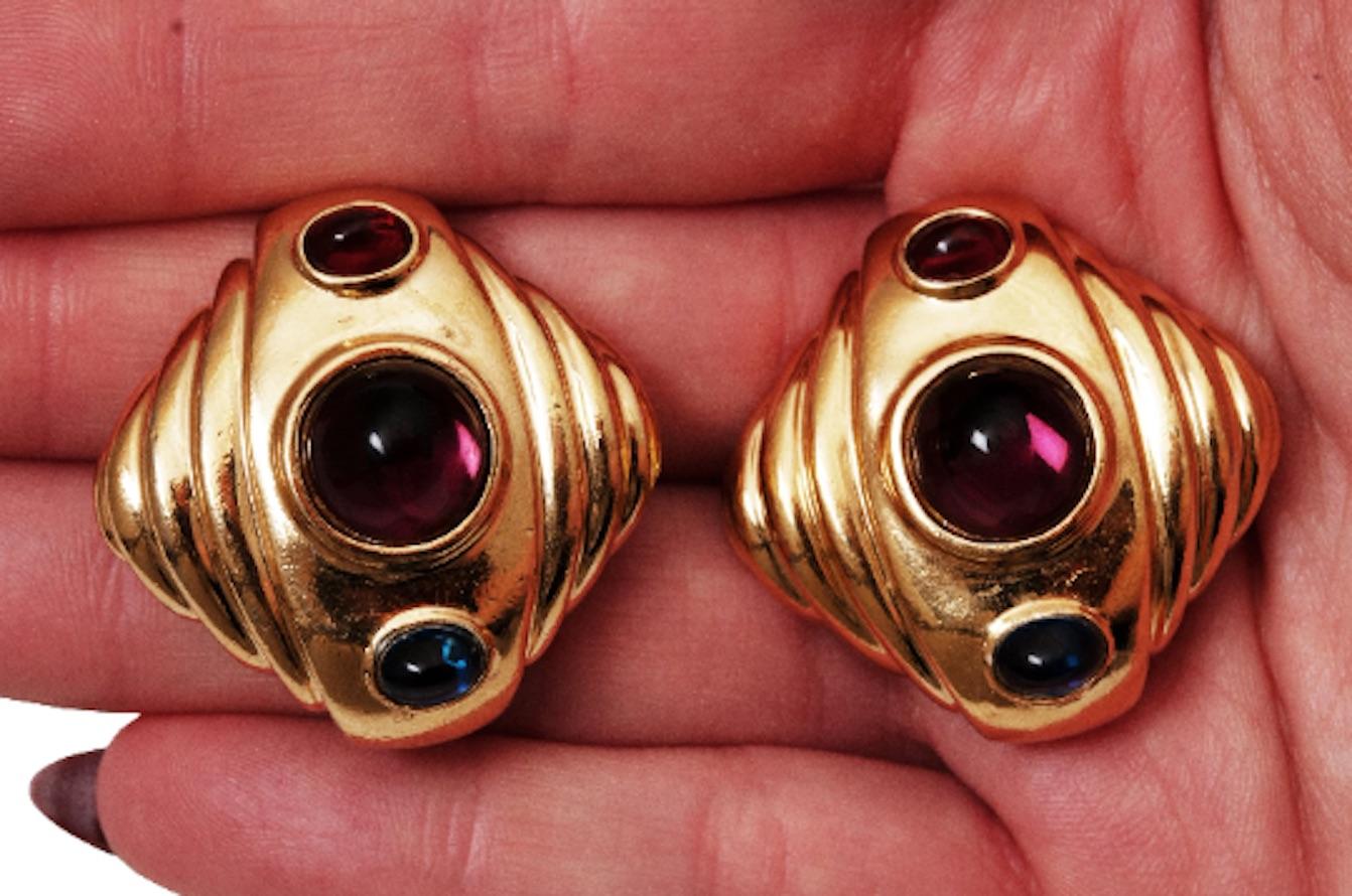 A statement pair of Ciner vintage clip-on earrings with two smaller red and blue oval cabouchon glass stones emulating ruby and sapphire and a large purple domed cabouchon reprensenting amethyst.  Richly set in gold plated base metal with a steped