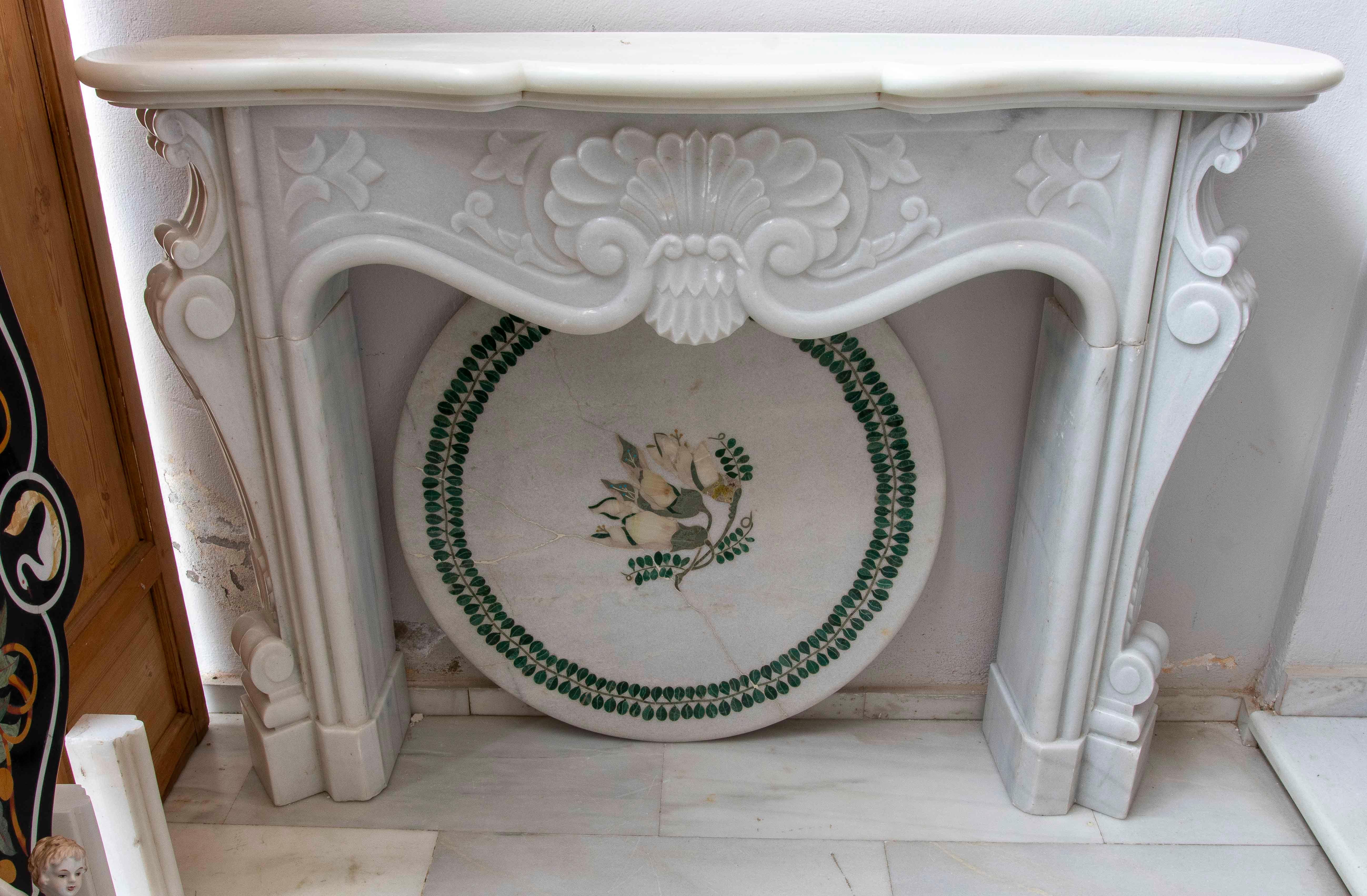 A sophisticated fireplace crafted from white marble with delicate, classically inspired ornamental carvings. Its design features a molded upper mantel with wavy lines, while the front displays floral motifs, acanthus leaves, and geometric elements