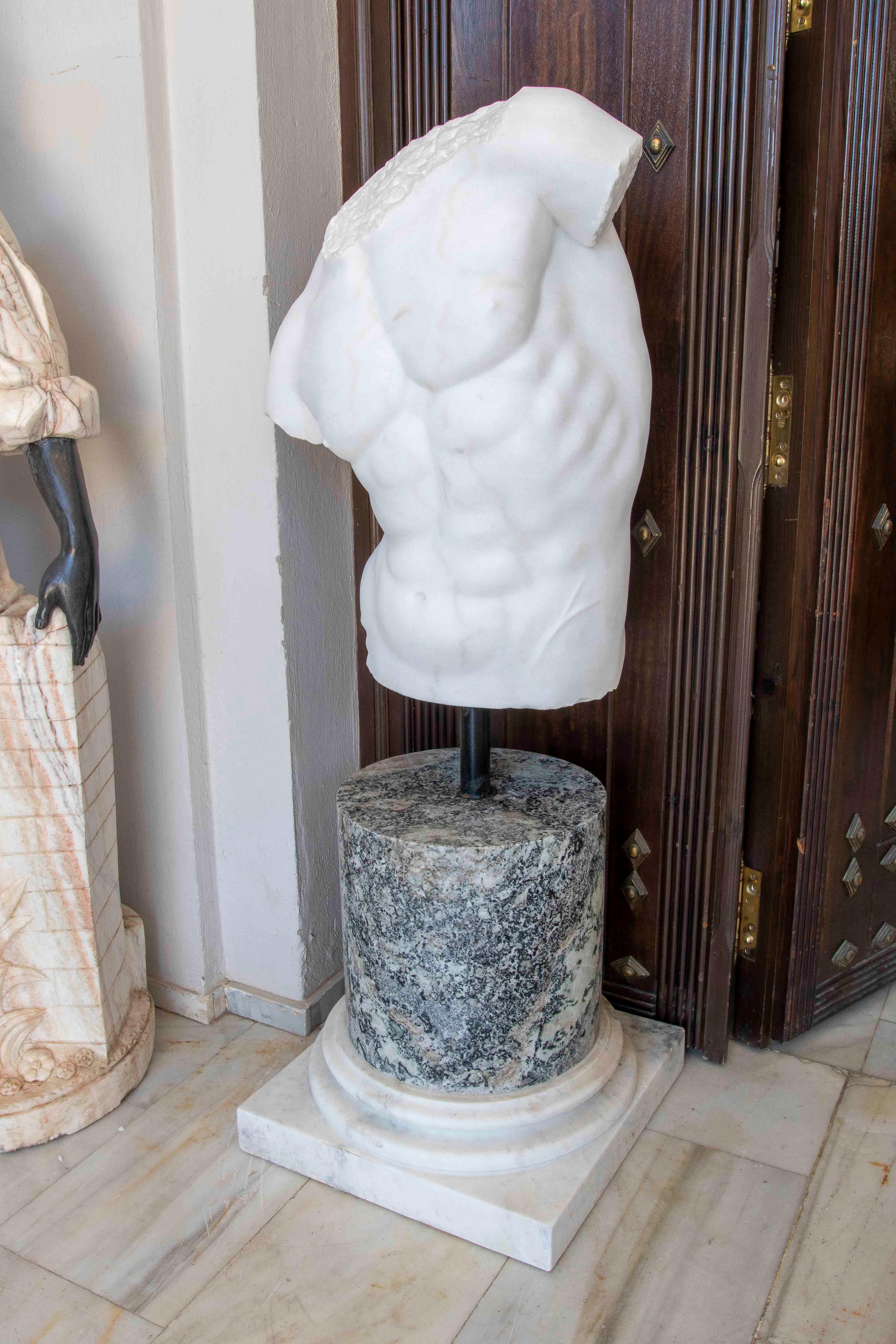 An imposing male torso sculpted in white marble, inspired by the classical aesthetic of Greco-Roman sculpture. The piece features refined anatomical work, highlighting the chest and abdominal muscles with great realism and sculptural strength. Its